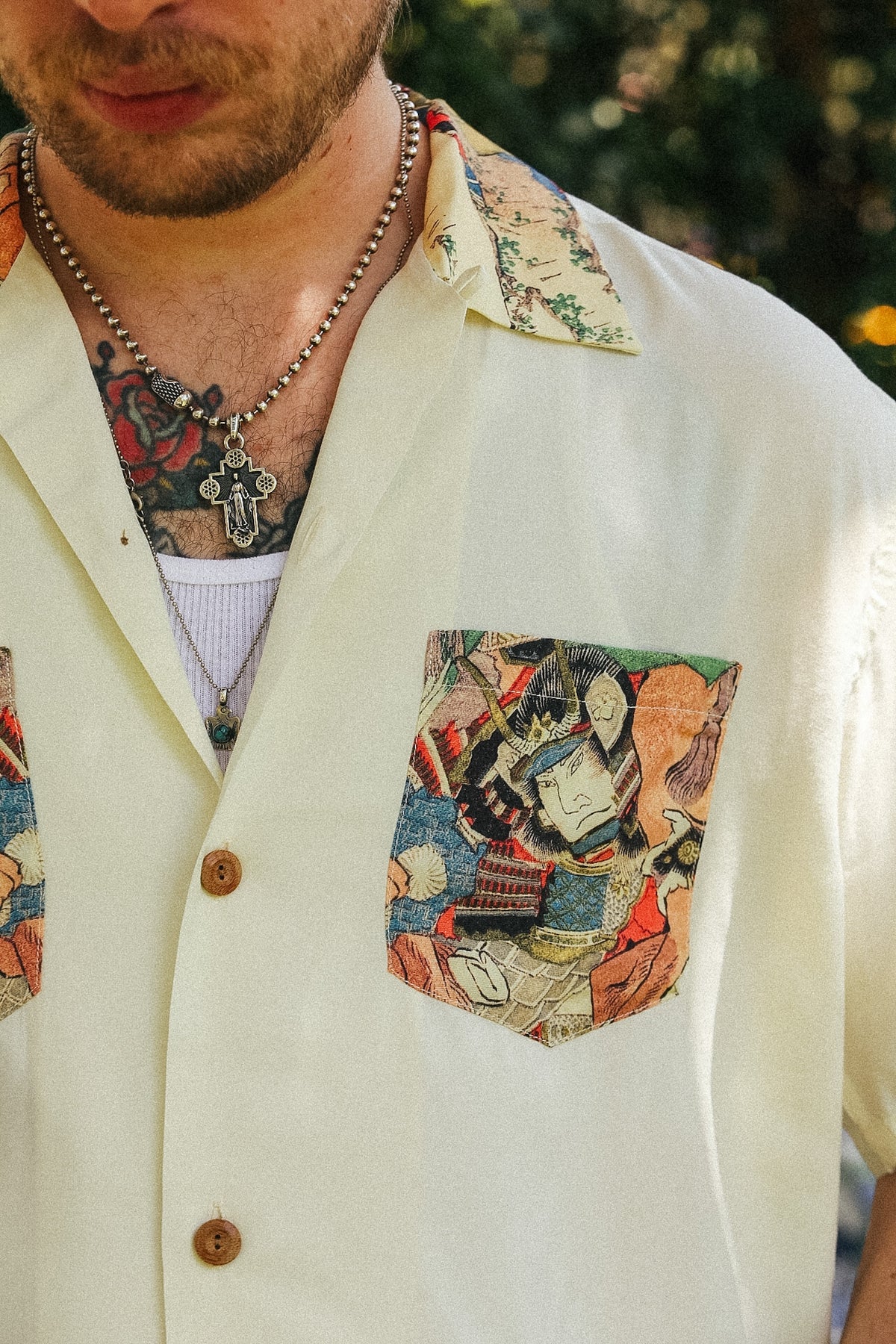Close-up of a man wearing a cream-colored short-sleeve button-up shirt with a multicolor abstract-patterned chest pocket and matching patterned collar.