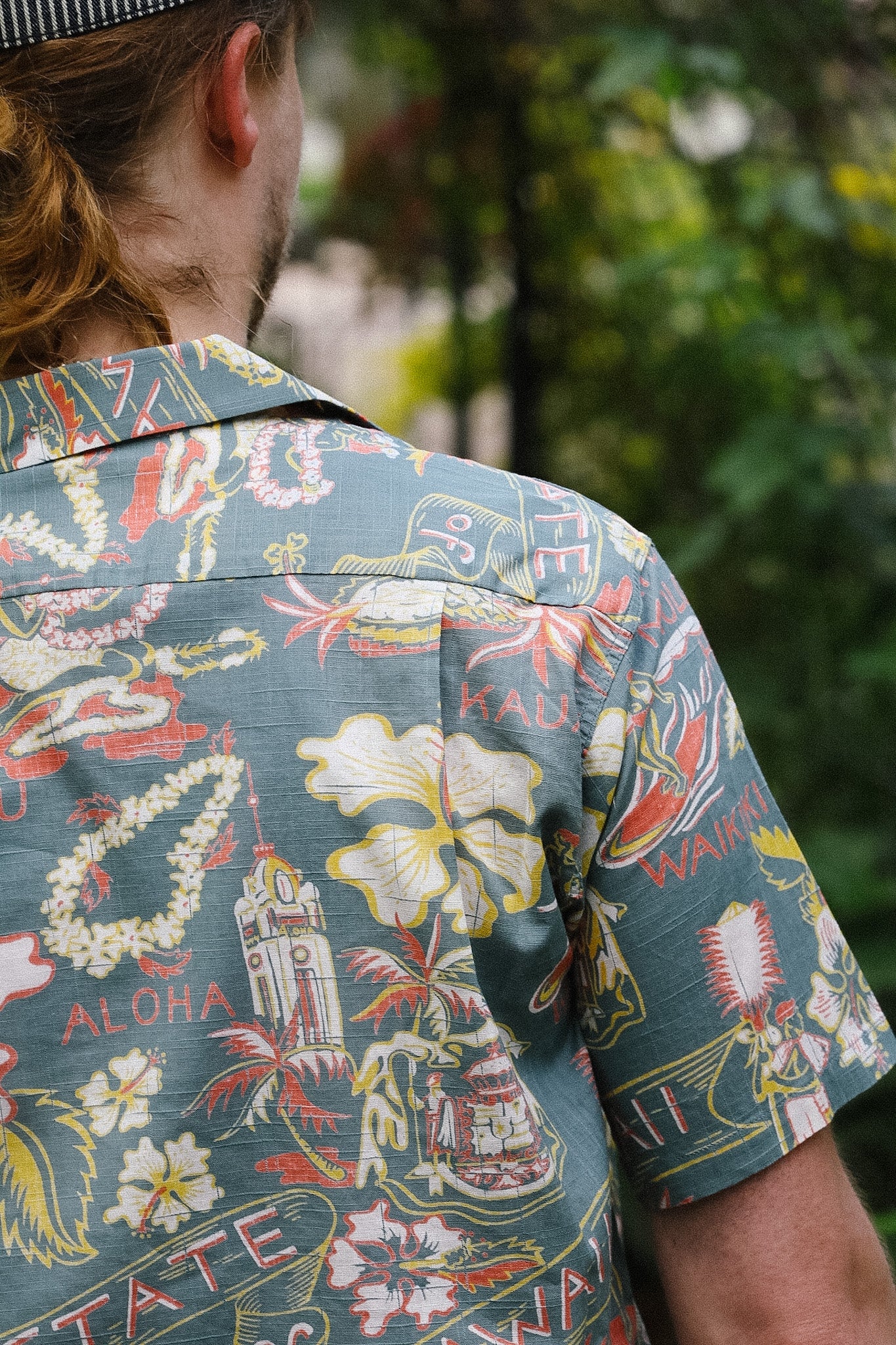 Person wearing a colorful Hawaiian shirt with various designs and text.