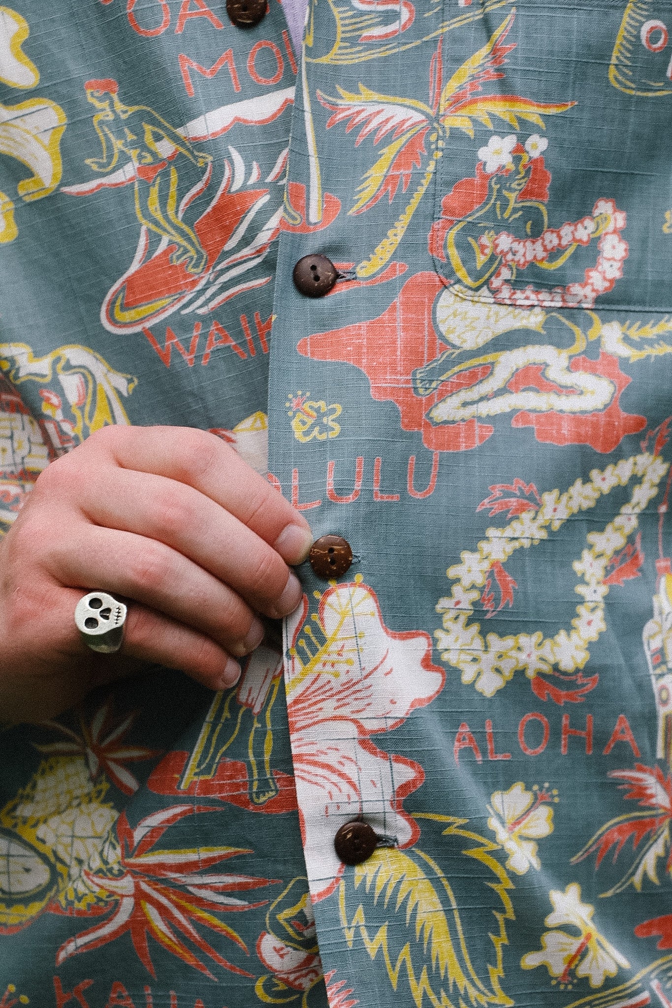 Hawaiian shirt with colorful graphics and text, held by a hand.