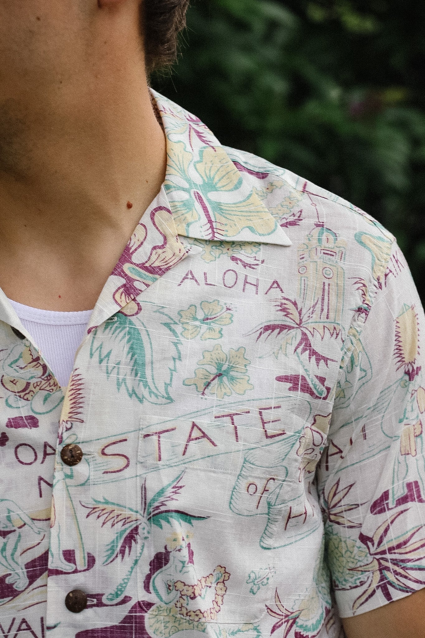 Close-up of a person wearing a colorful Hawaiian shirt with floral patterns and text.