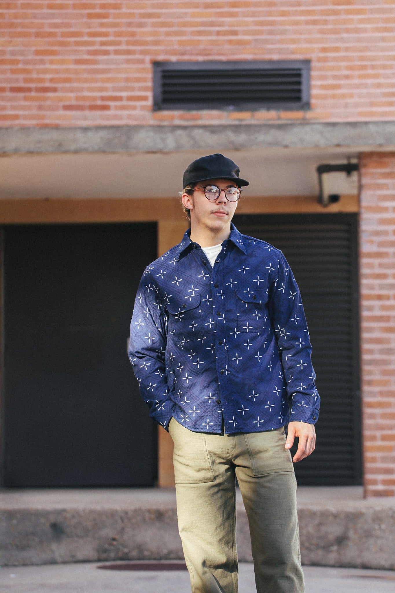 Man wearing indigo Narihirabishi goldfish pattern jacquard work shirt with beige pants and black cap outdoors