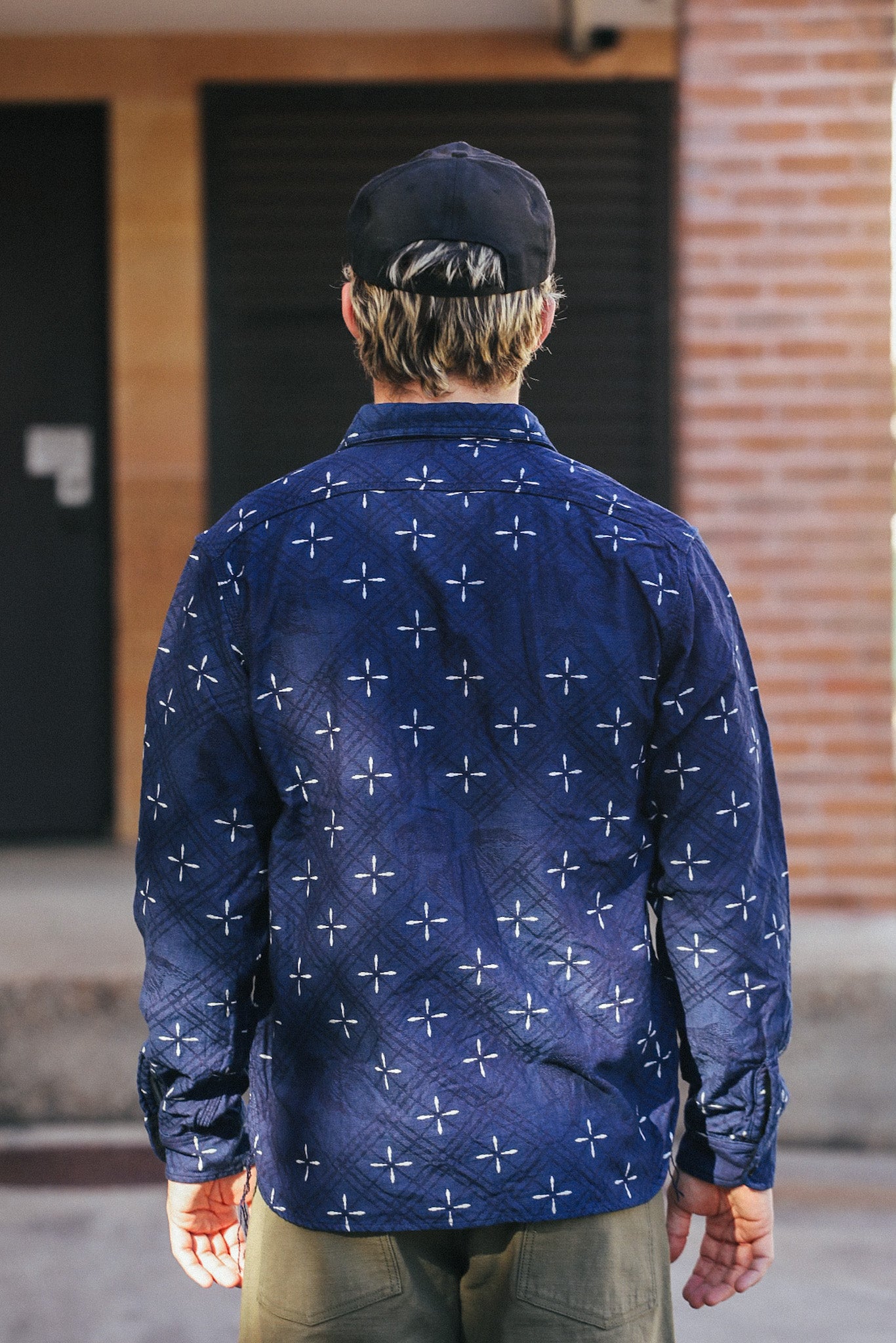 Man wearing indigo Narihirabishi Goldfish Pattern jacquard work shirt and black cap, standing outdoors