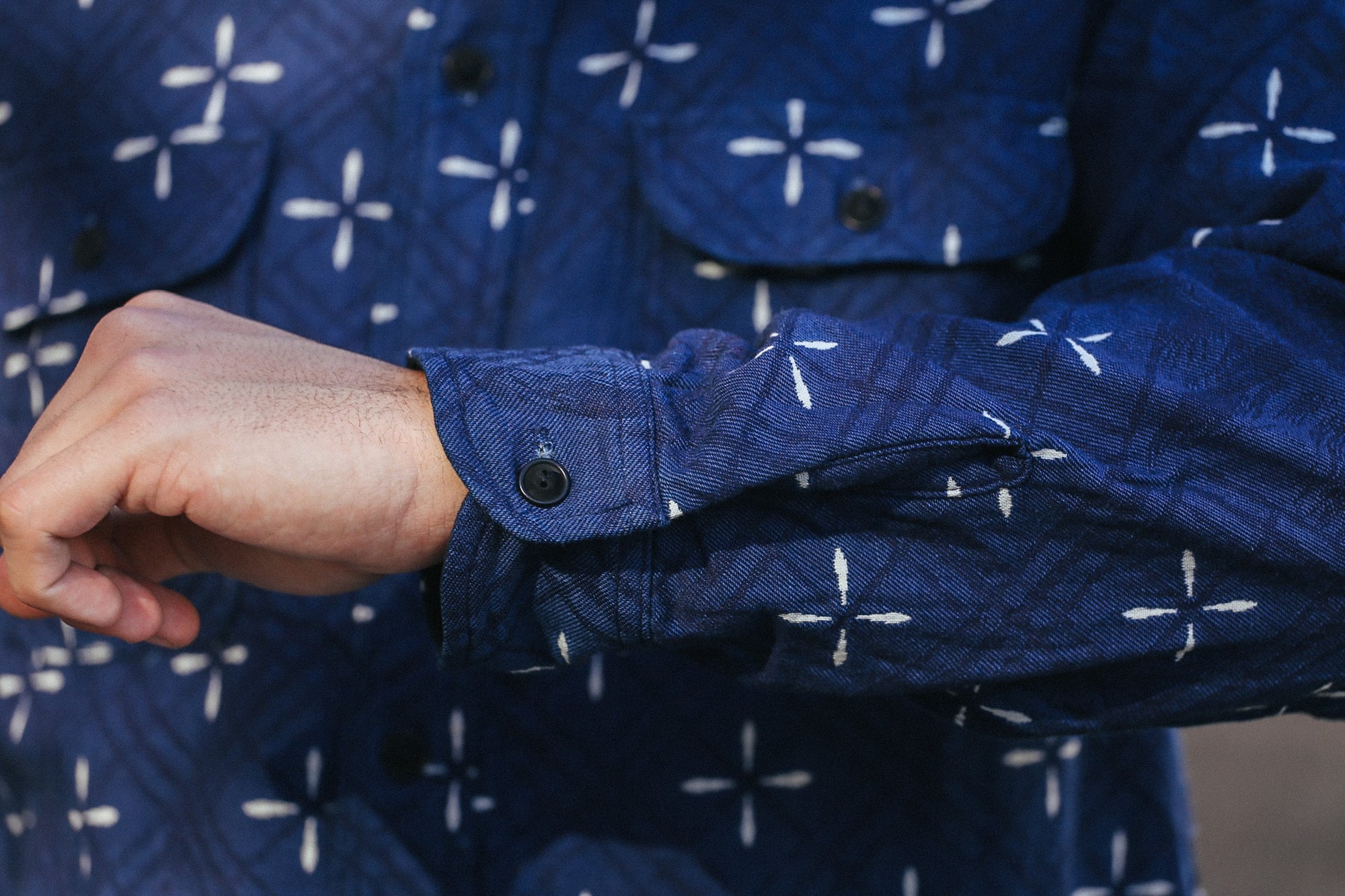 Close-up of indigo jacquard work shirt sleeve with white cross pattern and black button detail