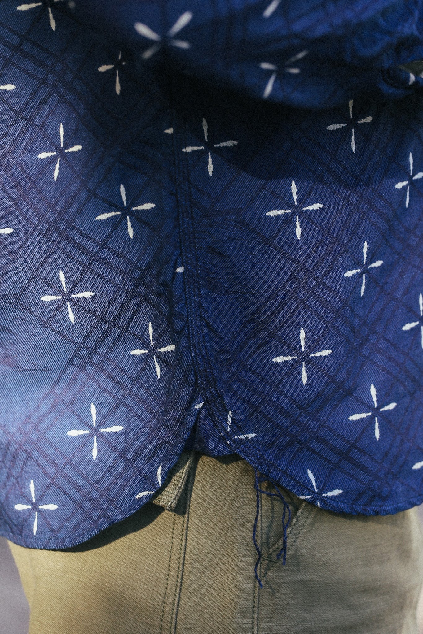 Close-up of indigo jacquard work shirt with Narihirabishi goldfish pattern and visible stitching over beige pants