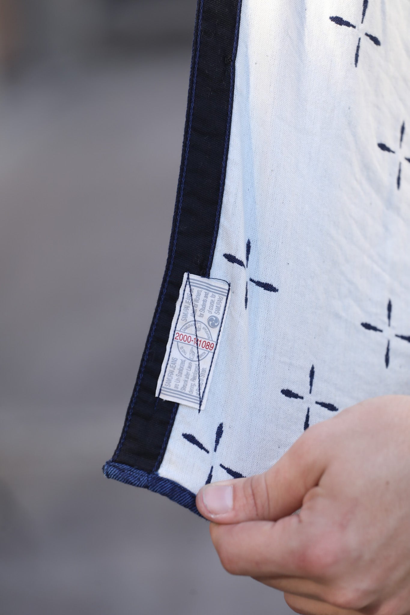 Close-up of hand holding indigo blue and white fabric with navy trim and sewn label showing red and black text