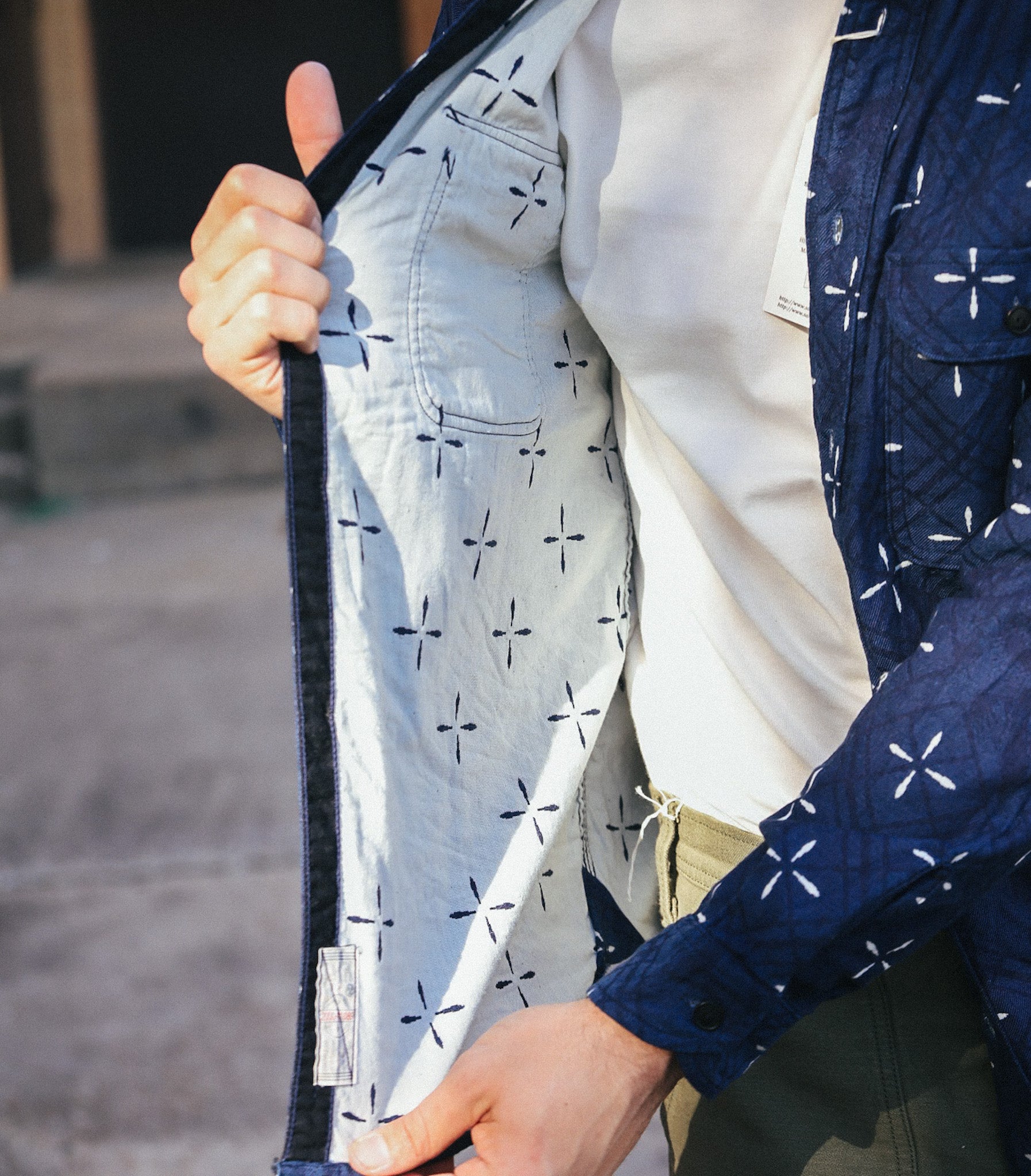 Close-up of a person wearing an indigo jacquard work shirt with white cross pattern and showing the inner light-colored lining with similar pattern
