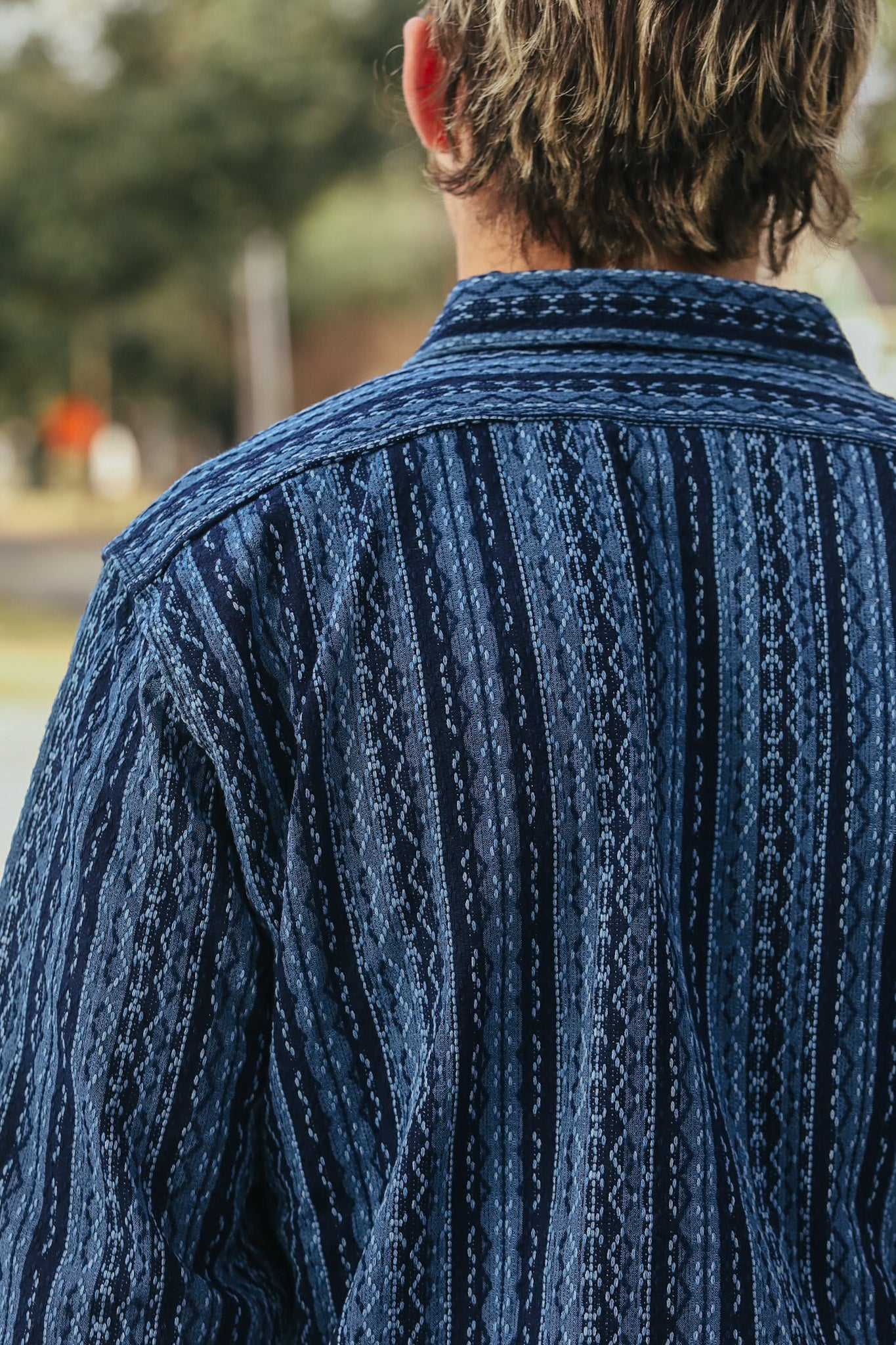 Person wearing a blue patterned shirt with a blurred outdoor background