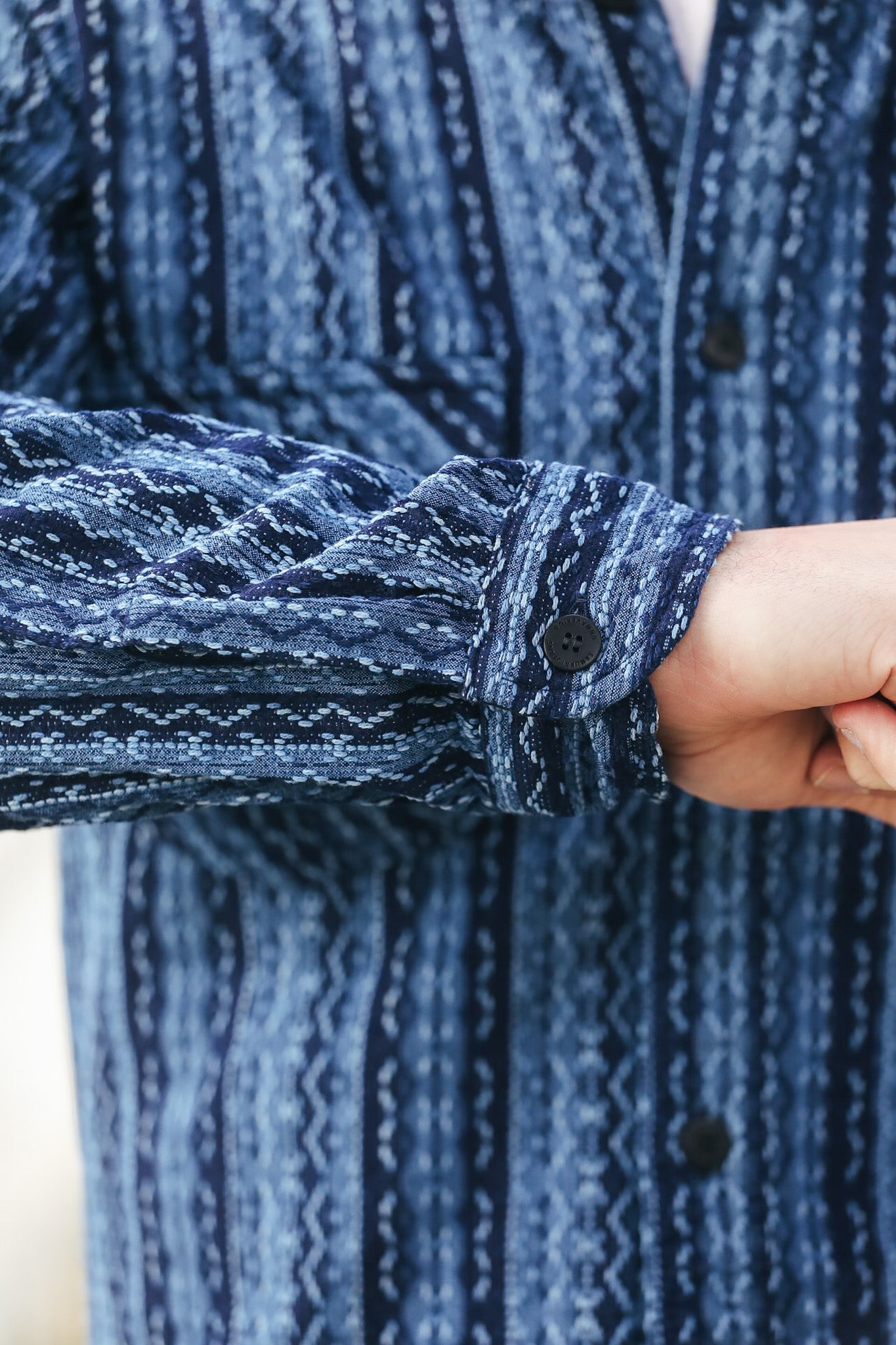 Close-up of a person wearing a blue patterned shirt with a focus on the sleeve and collar.