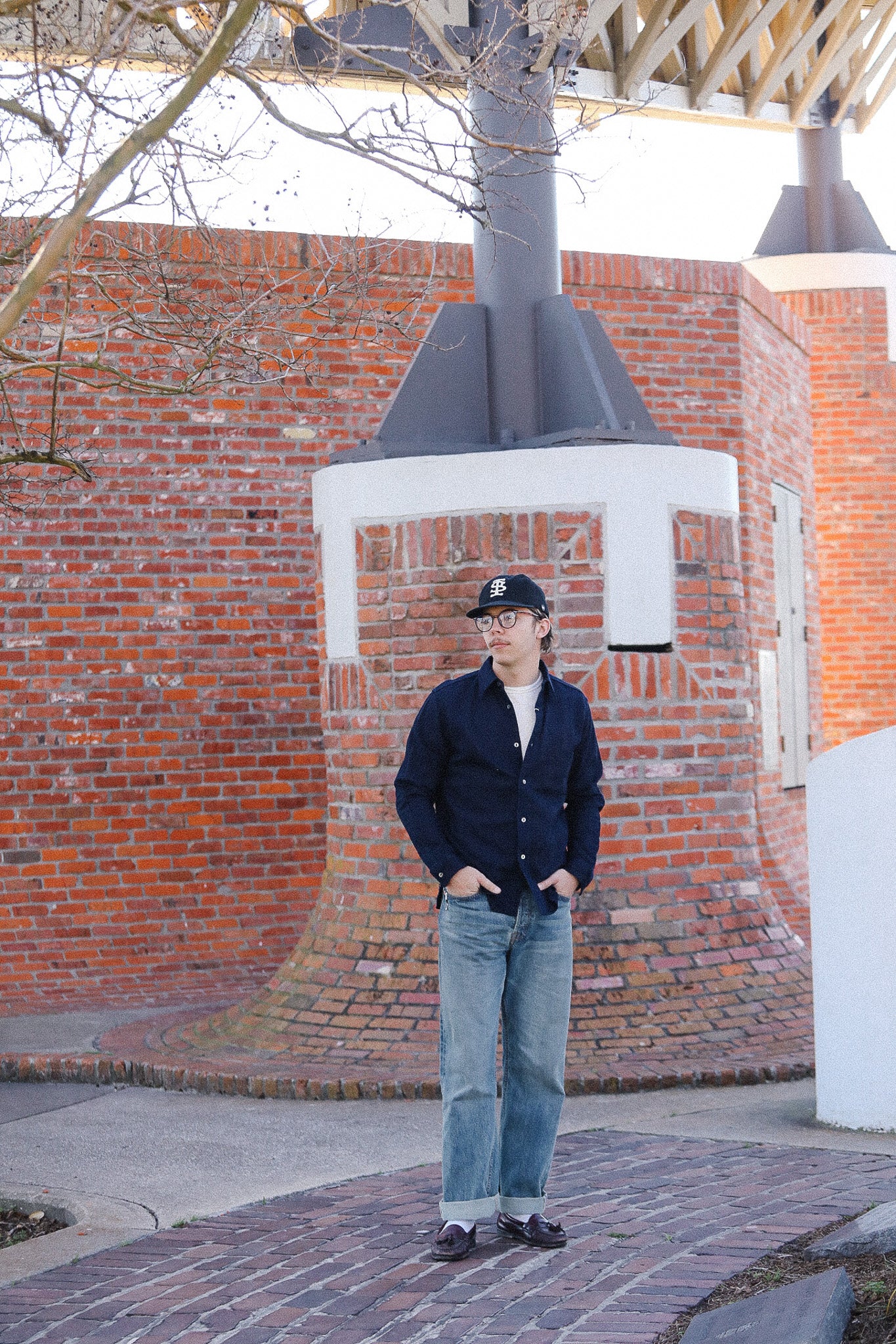 Person standing in front of a brick wall with a large outdoor sculpture.