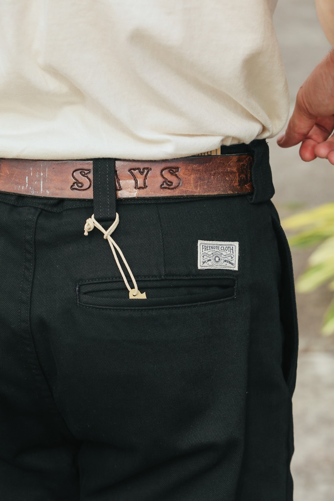 Person wearing black pants with a visible brand logo, white shirt, and brown belt.