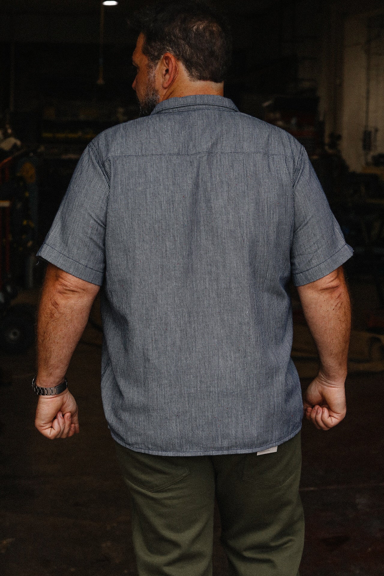Man wearing short sleeve rainbow nep hickory stripe shirt in a workshop setting
