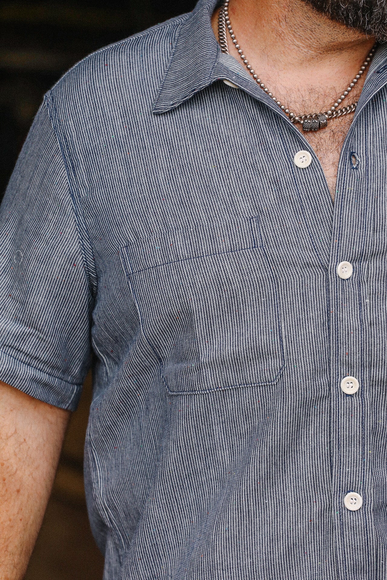 Close-up of man wearing blue and white striped short sleeve button-up shirt with chest pocket and silver necklace