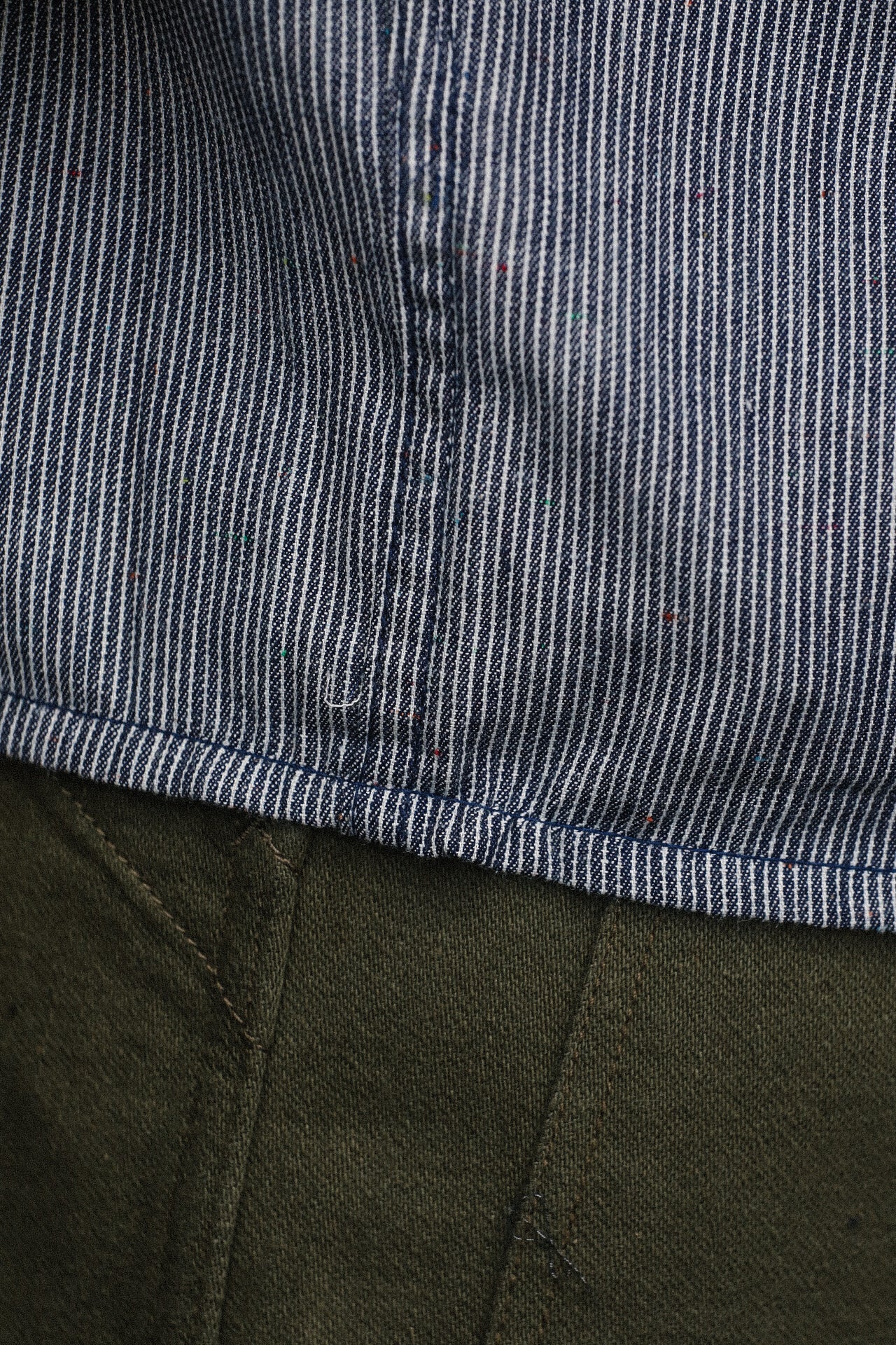 Close-up of striped blue and white short sleeve shirt hem with colorful specks above olive green pants stitching