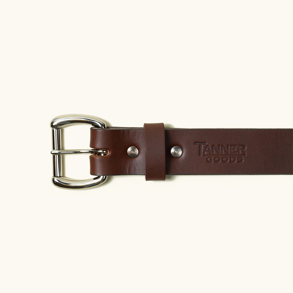 Cognac leather belt with silver buckle and embossed Tanner Goods logo on light background