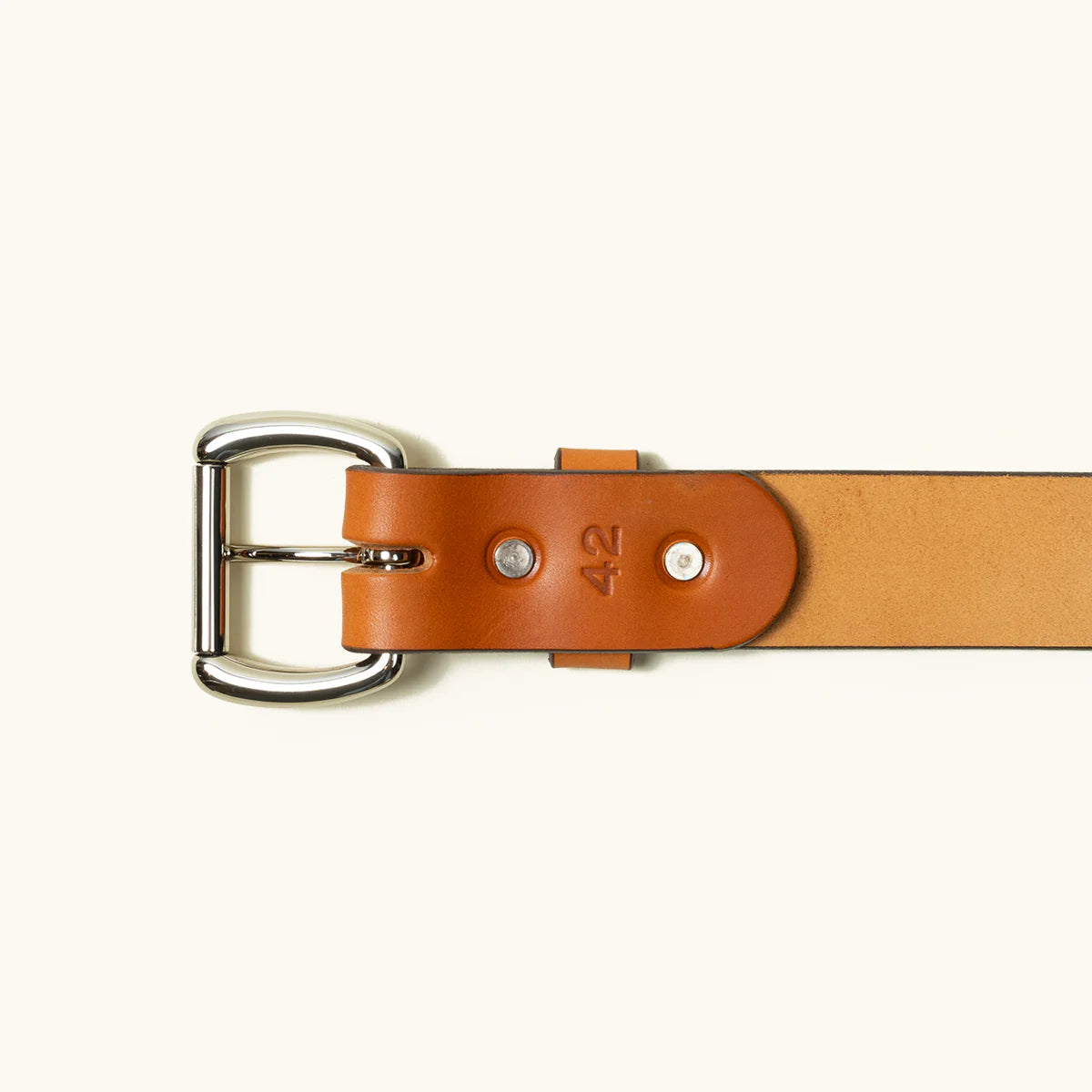 Close-up of tan leather belt with silver metal buckle and size 42 stamped on saddle bottom