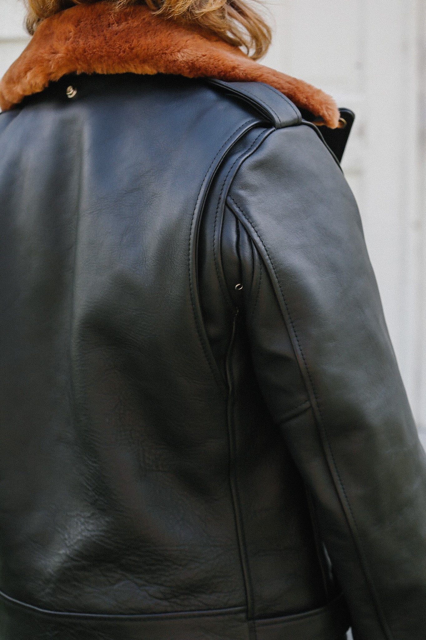 Back side of a black saddle dyed horsehide leather riders jacket with a brown fur collar