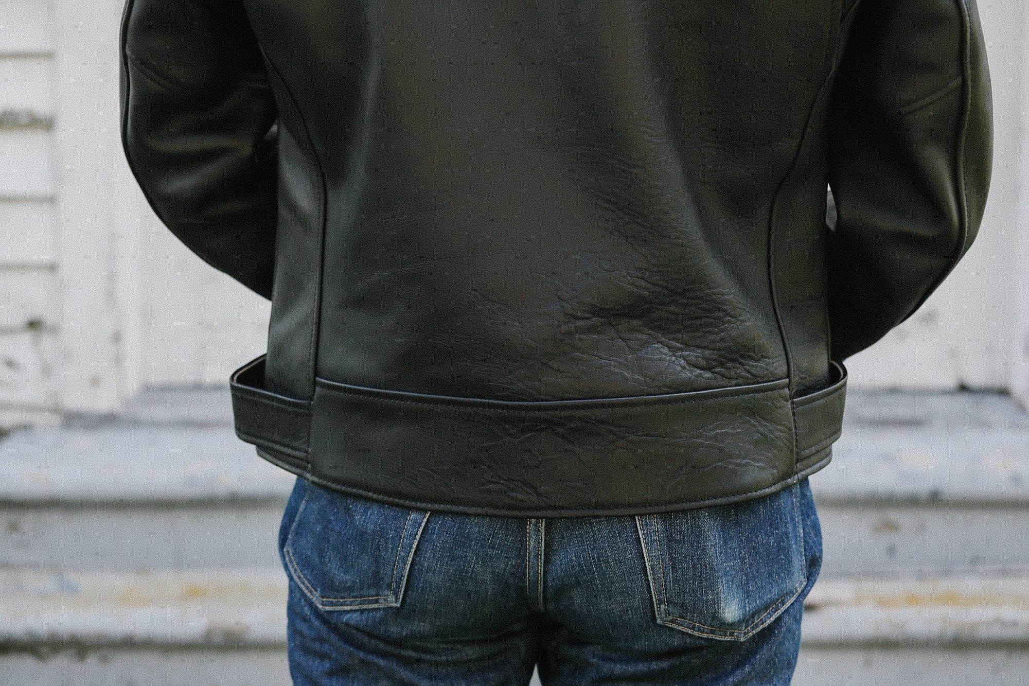 Close-up of black sumiyaki dyed double riders leather jacket on person wearing blue jeans standing outdoors