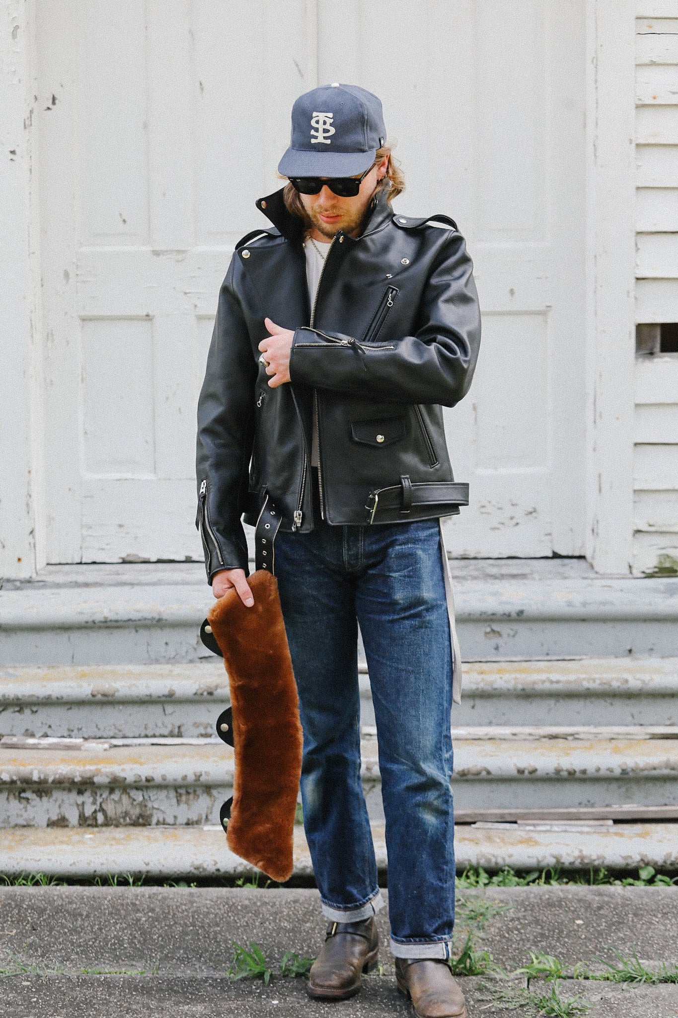 Man wearing black horsehide leather double riders jacket and jeans holding brown fur collar accessory outdoors