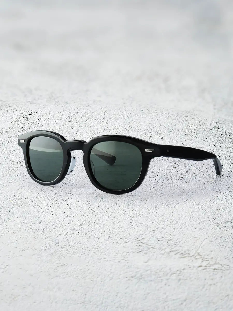 Black sunglasses with green lenses on a textured white surface