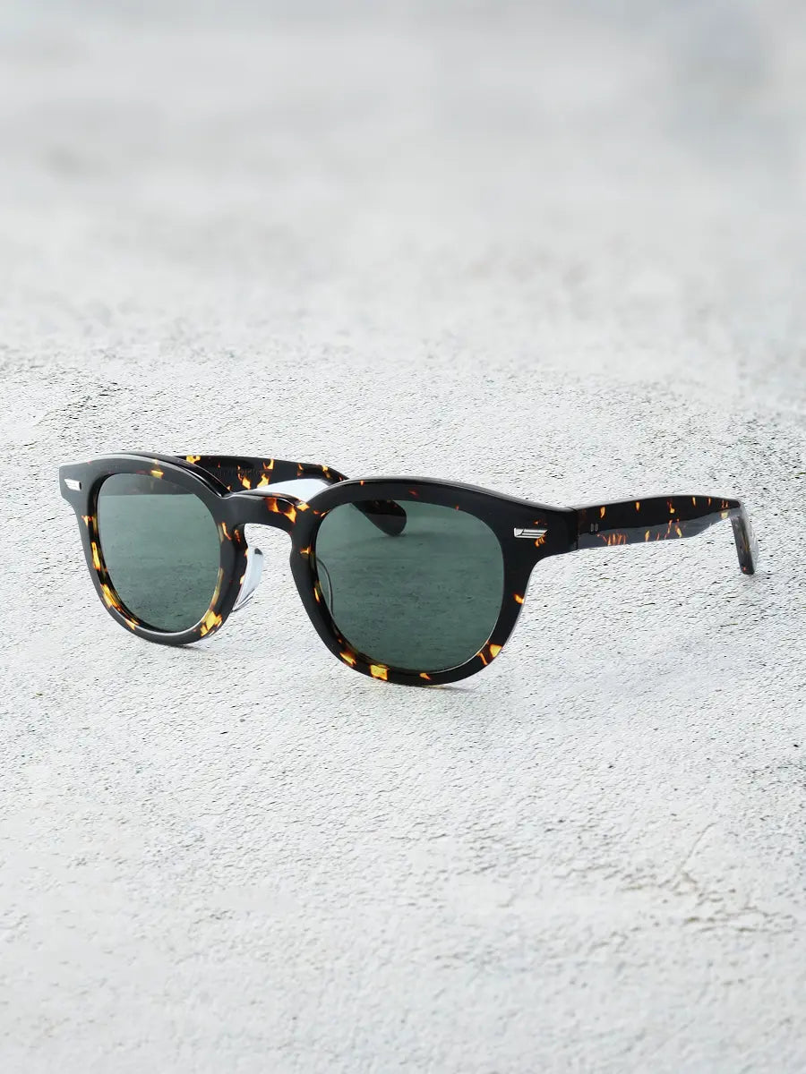 Sunglasses with tortoiseshell frame and green lenses on a textured white surface