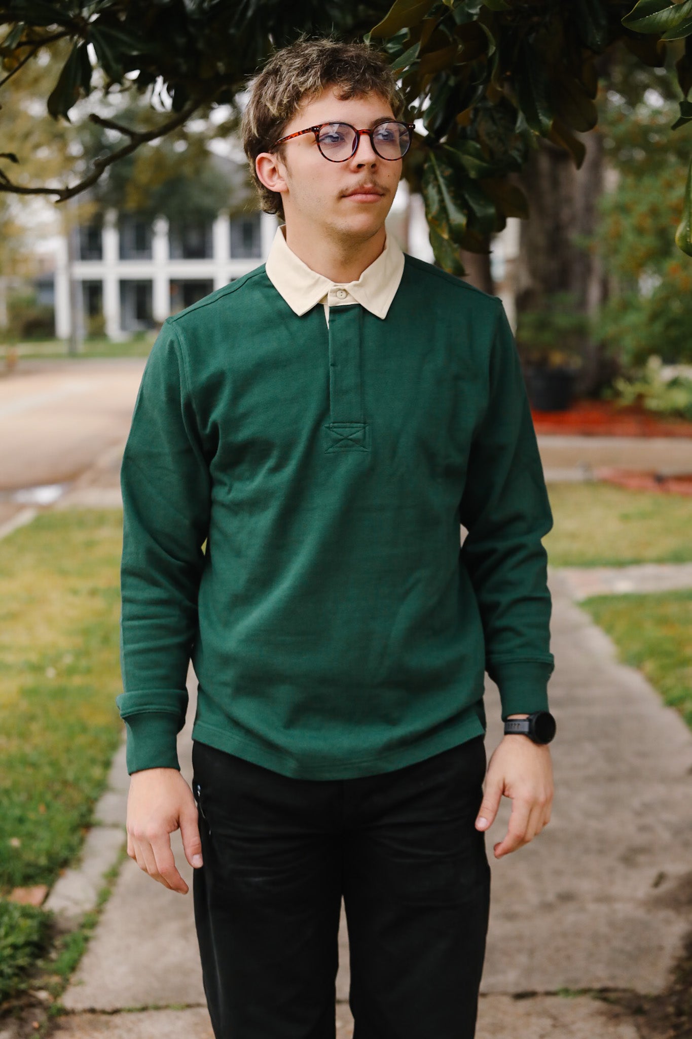 Person wearing a green sweater and black pants standing outdoors on a sidewalk.