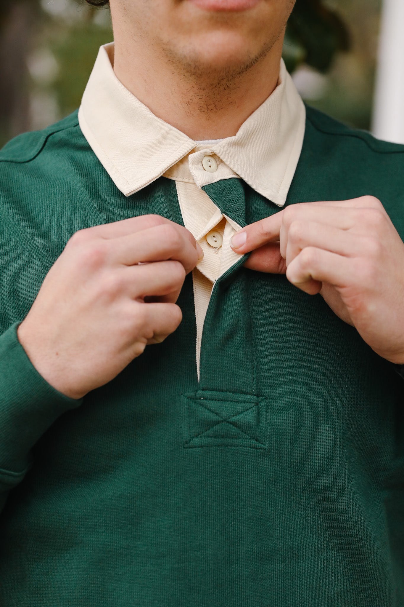 Person adjusting a button on a green shirt with a beige collar.