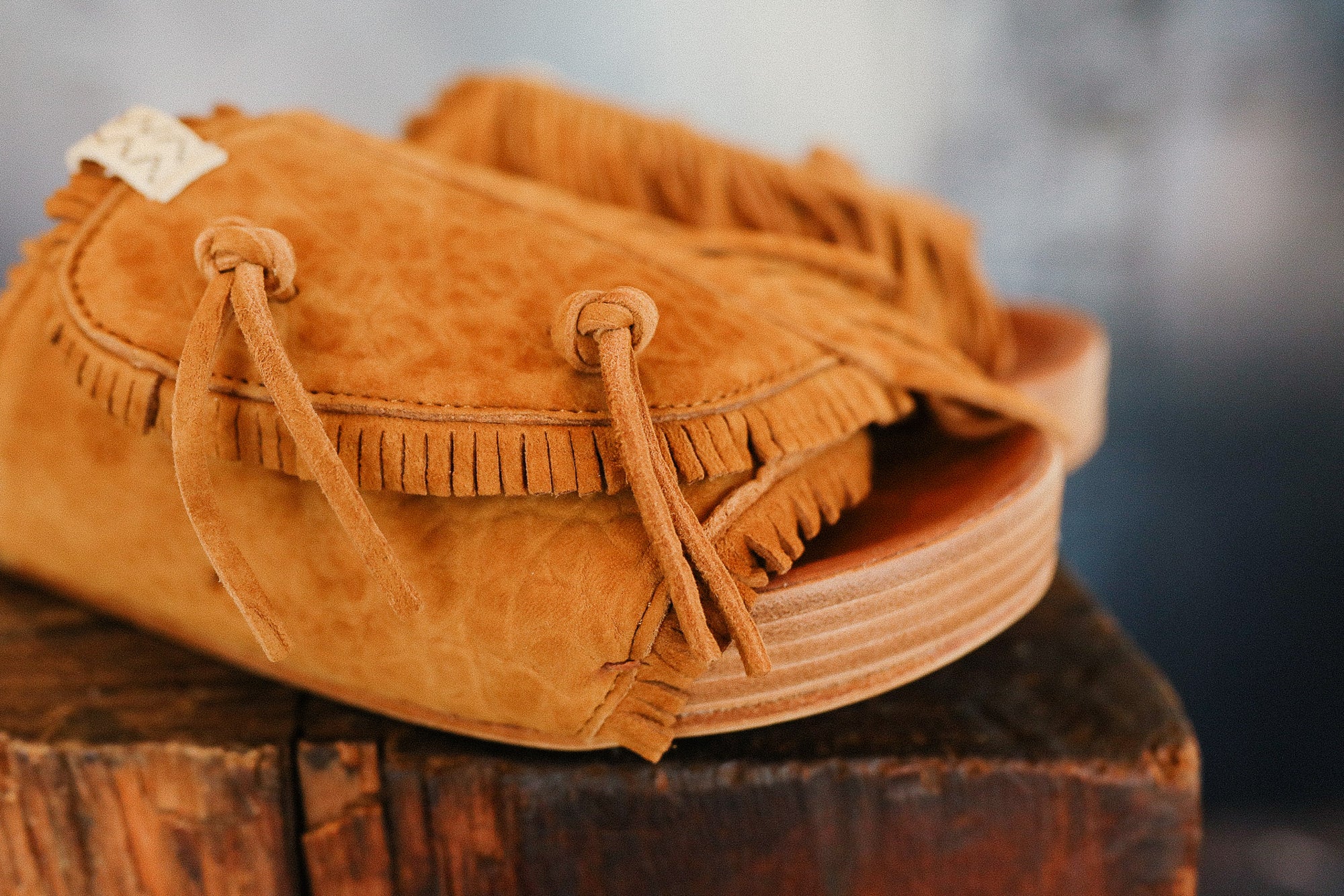 Brown suede sandal with fringes on a wooden surface