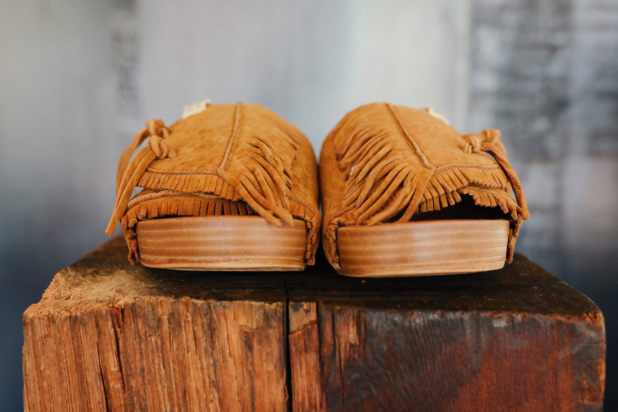 Pair of brown moccasins with fringes on a wooden block against a blurred background