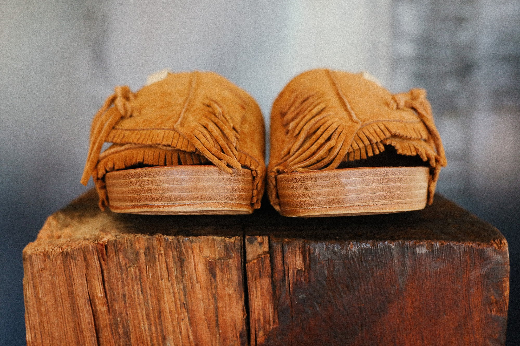 Pair of brown suede sandals on a wooden block with a blurred background