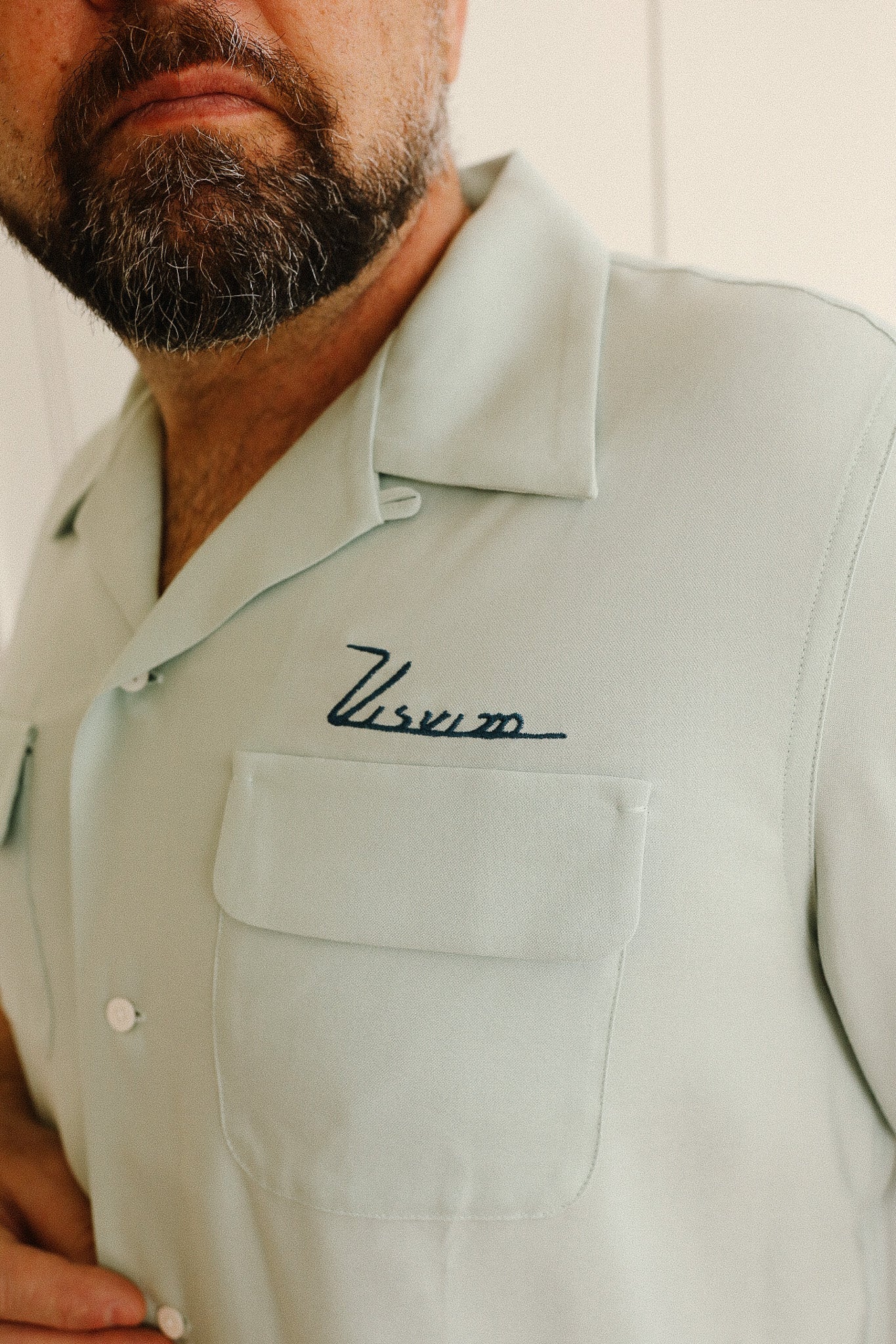 Light green shirt with a brand logo worn by a person, against a neutral background