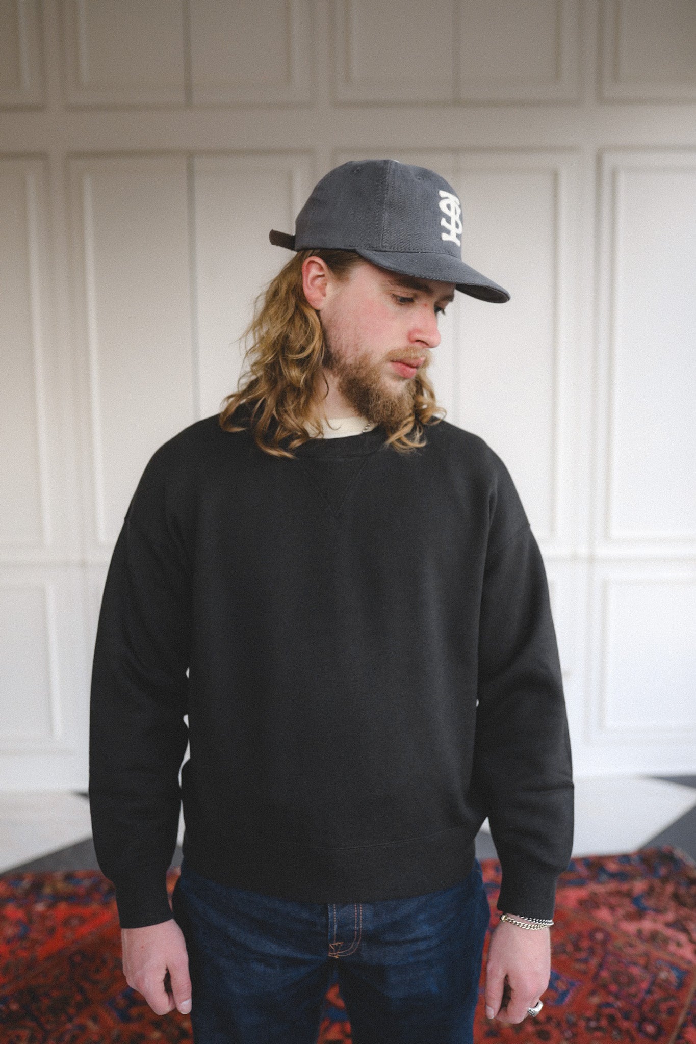 Man wearing a black sweatshirt and cap indoors with a neutral background