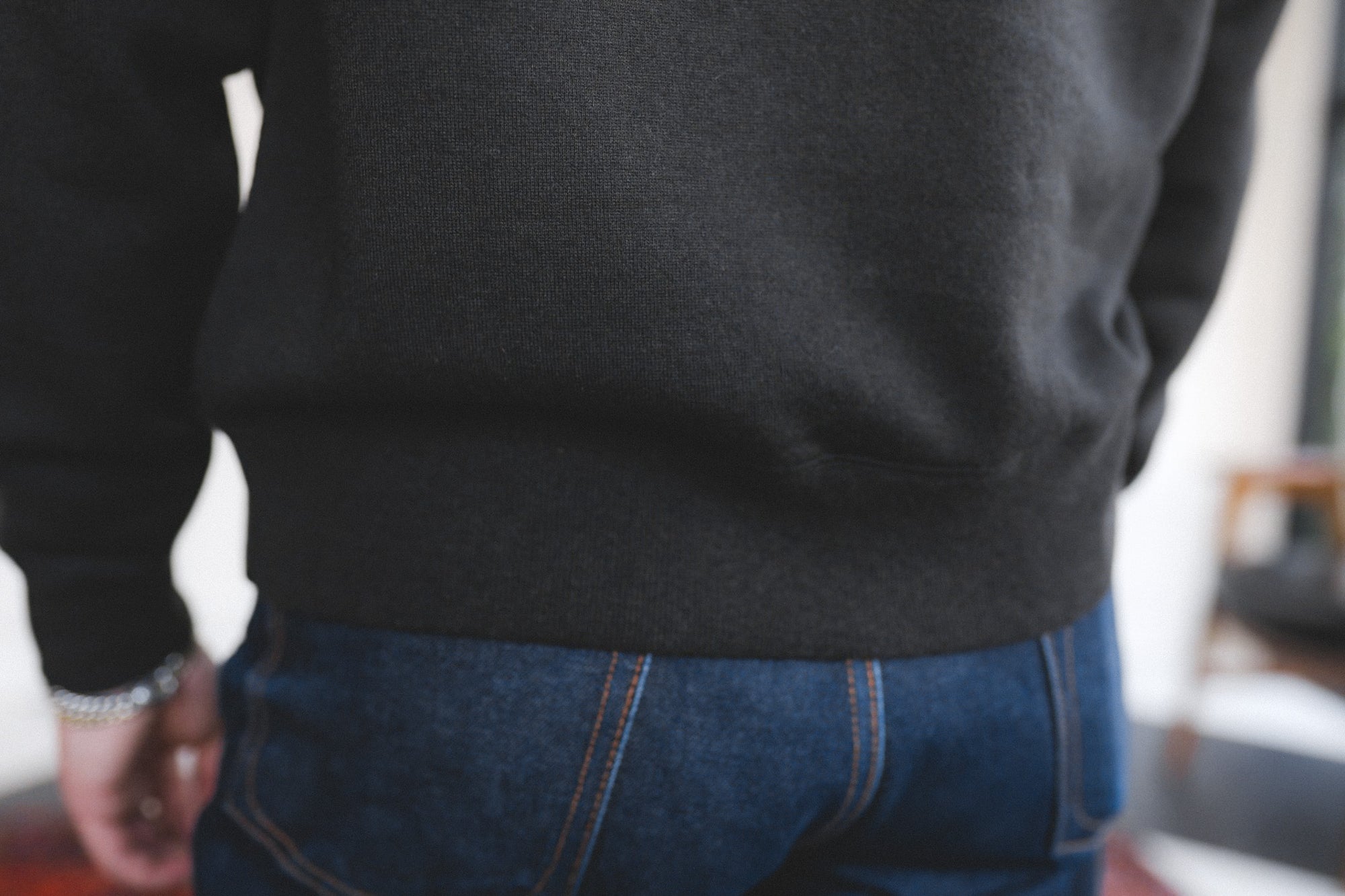 Person wearing a dark sweater and blue jeans with a blurred background