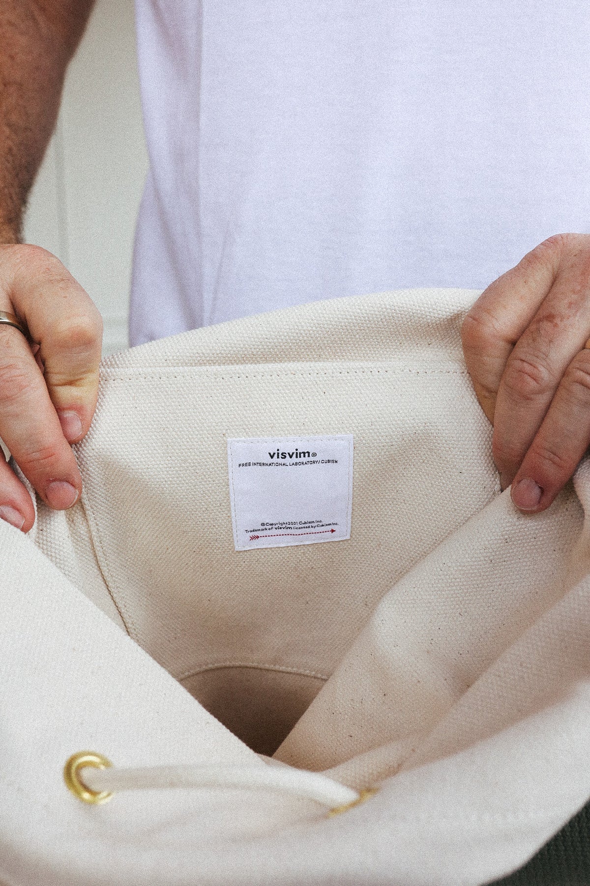 Close-up of a person holding an off-white canvas tote bag, showing the interior and a white sewn-in label that reads 'vievés'.