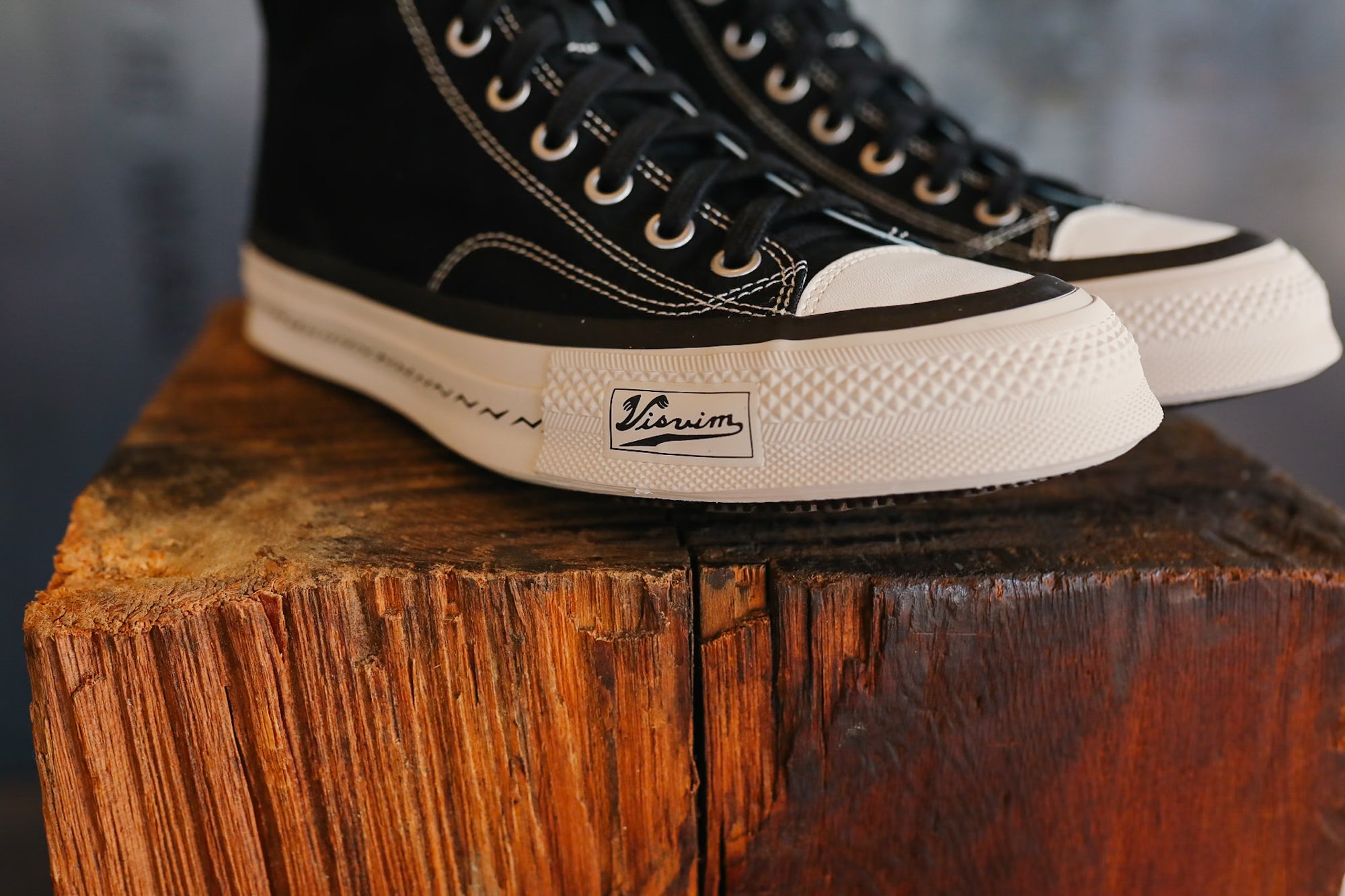 Black high-top sneakers with white soles on a wooden block