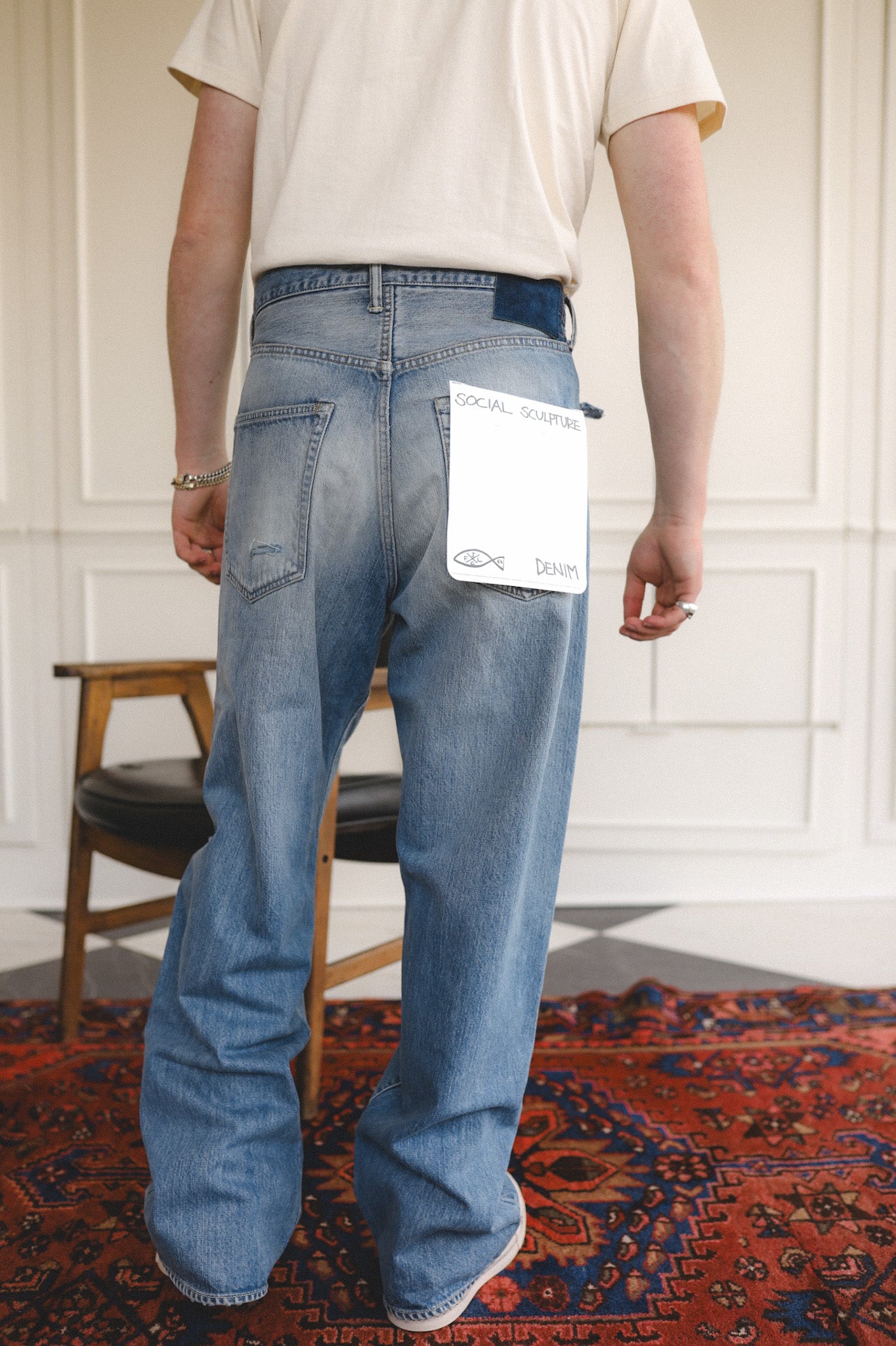 Person wearing blue jeans with a visible brand tag, standing on a patterned rug.