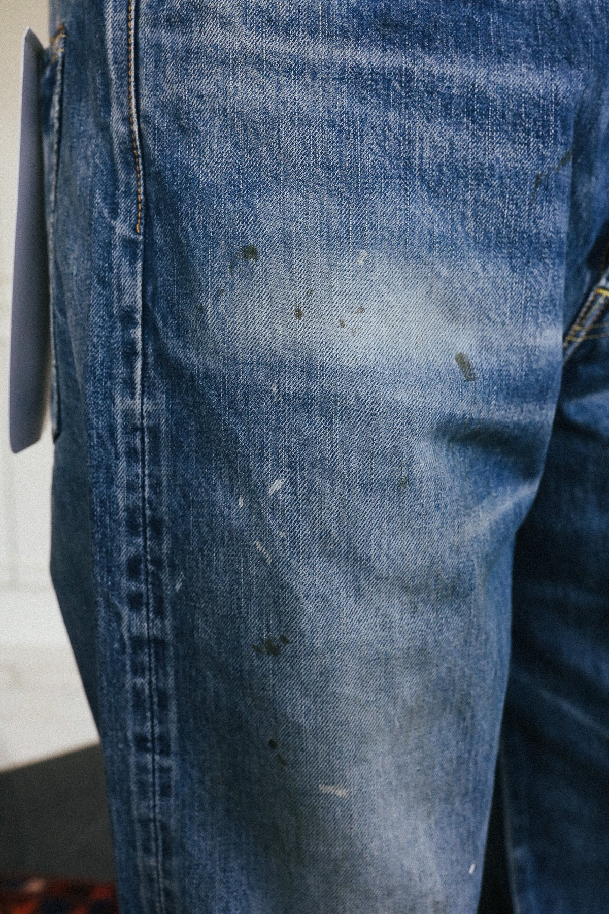 Close-up of a pair of blue denim jeans with visible dirt, stains, and scuffs on the thigh, showing the raw denim texture and stitching.