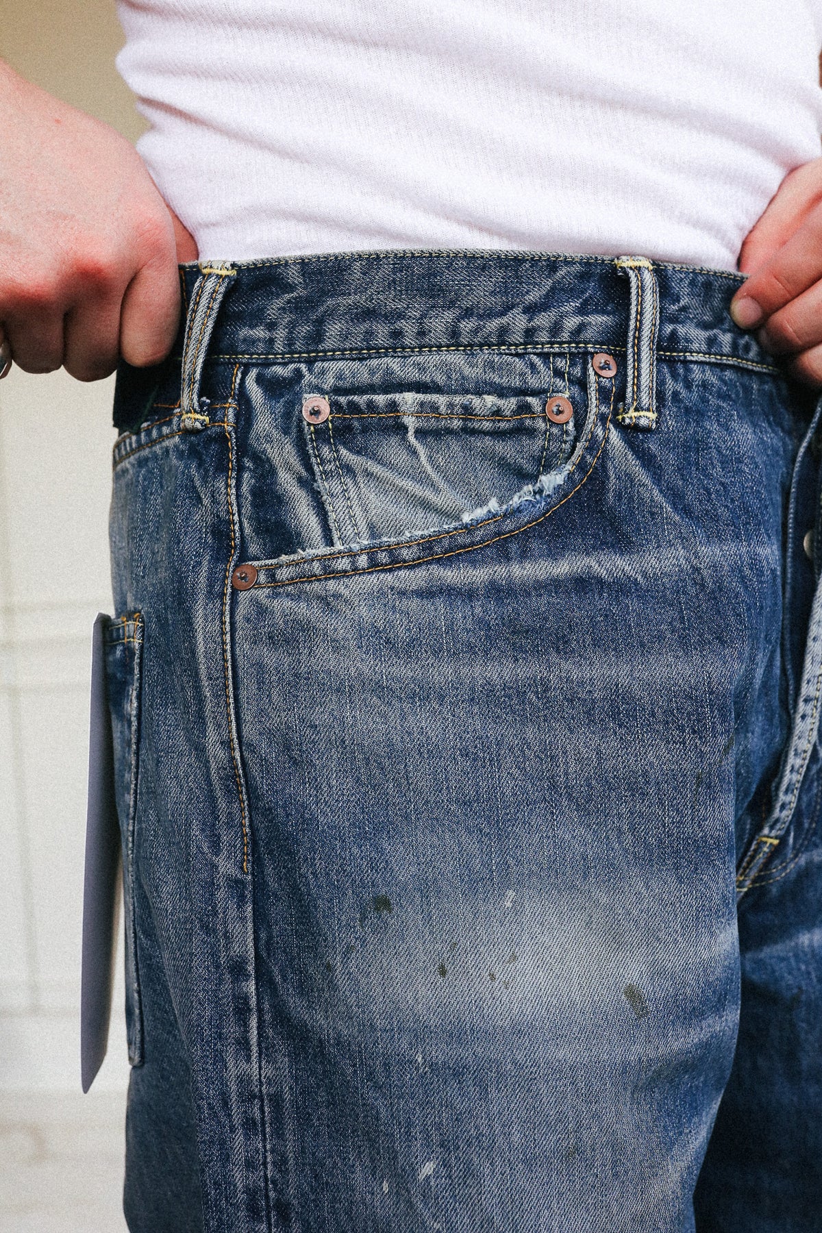 Close-up of a person wearing blue denim jeans with a white t-shirt, showing the back pocket and waistband details.