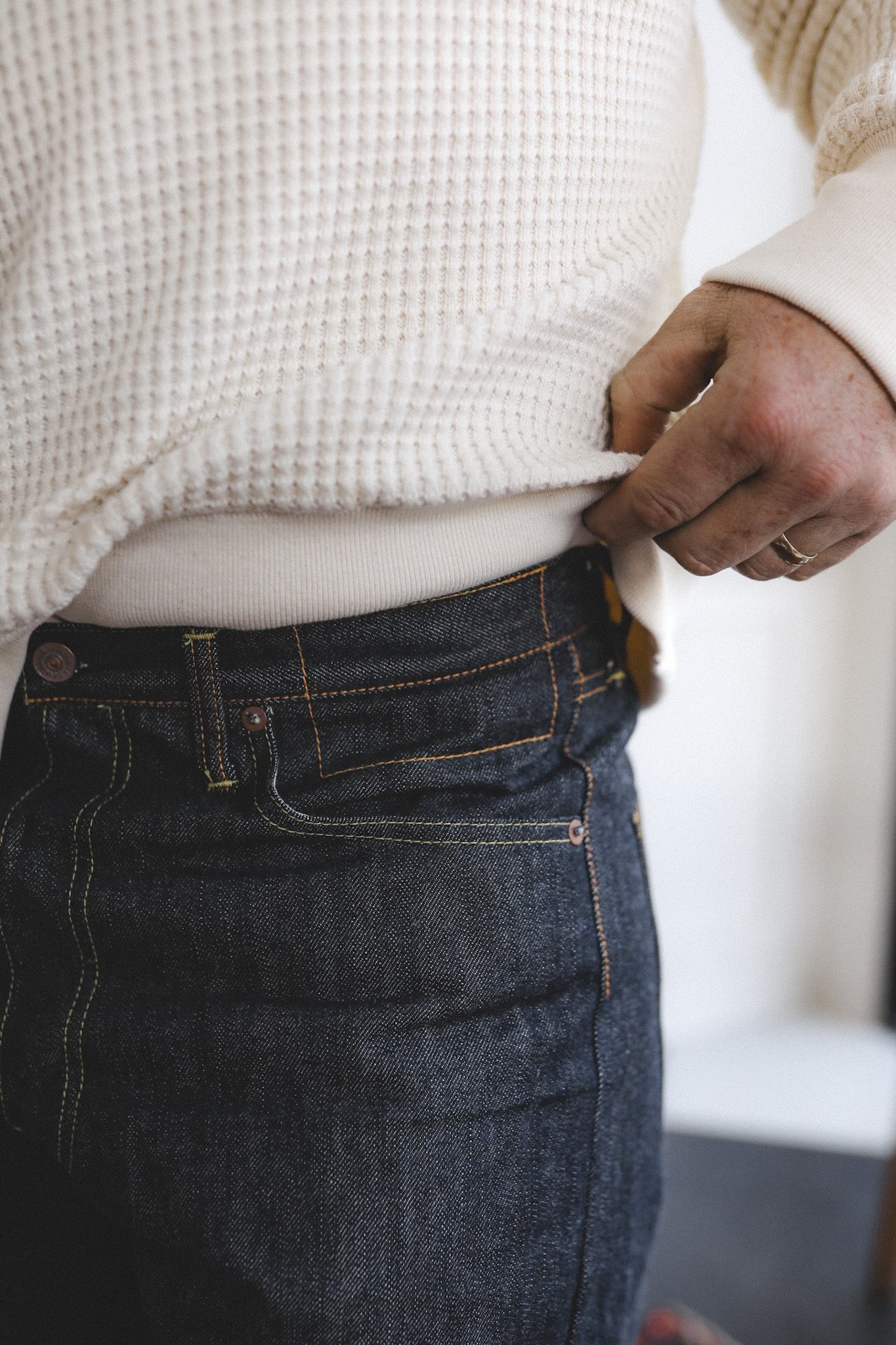 Person wearing a white textured sweater and dark blue jeans with a blurred background