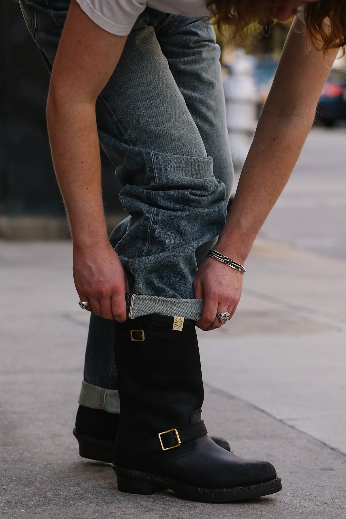 Person wearing blue jeans and black boots on a sidewalk.