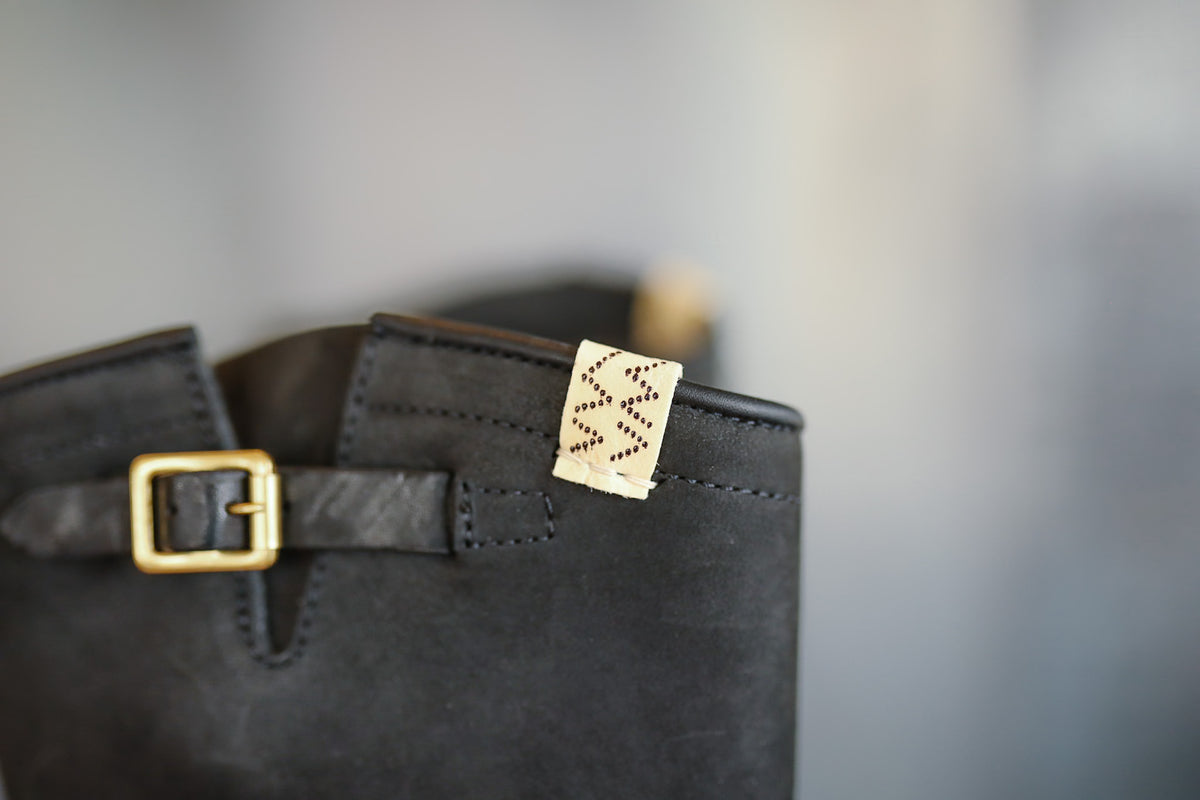 Close-up of a black leather bag with a gold buckle and tag on a blurred background
