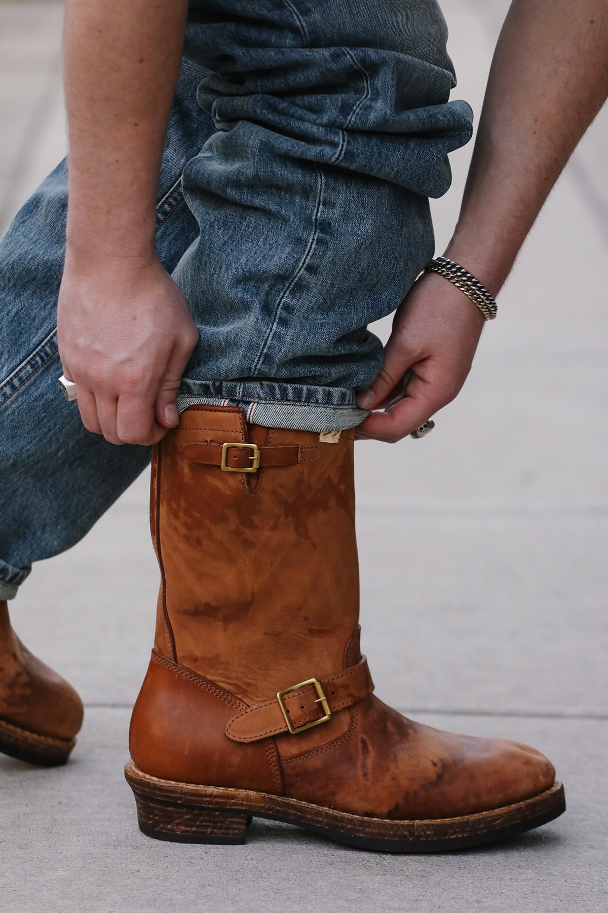 Person wearing brown leather boots with gold buckles on a light gray background