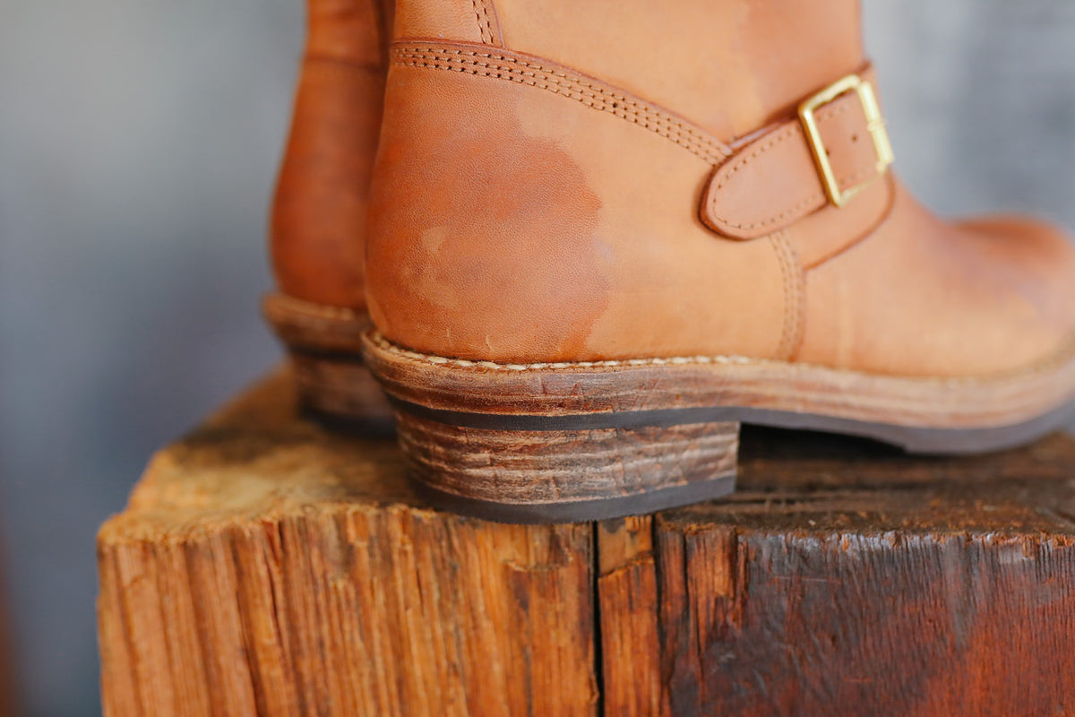 Pair of brown leather boots with a buckle on a wooden block against a blurred background