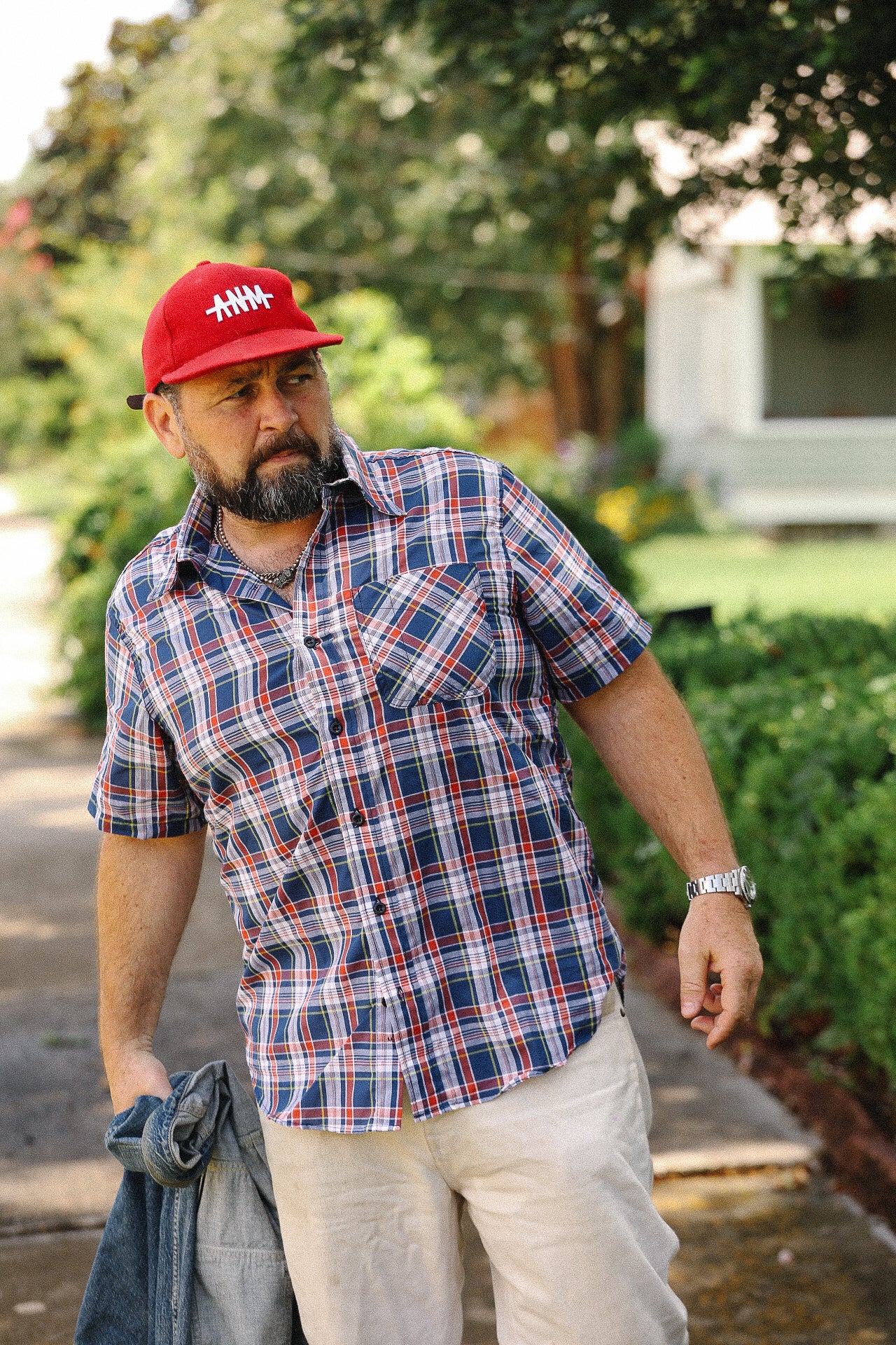 Man wearing Tellason navy Madras short sleeve plaid shirt with red cap and beige pants outdoors