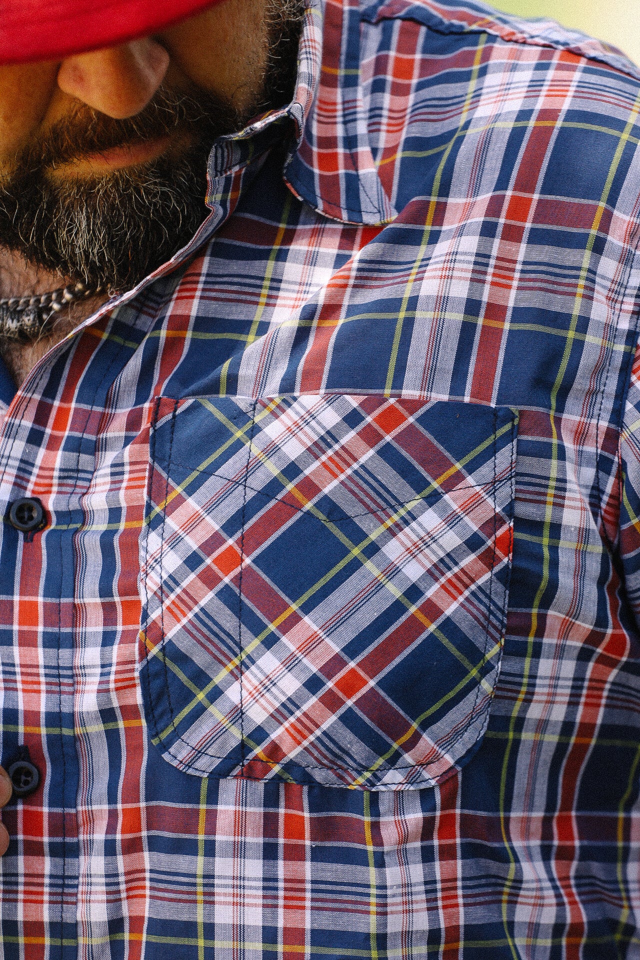 Close-up of man wearing navy, red, and white plaid short sleeve shirt with front chest pocket