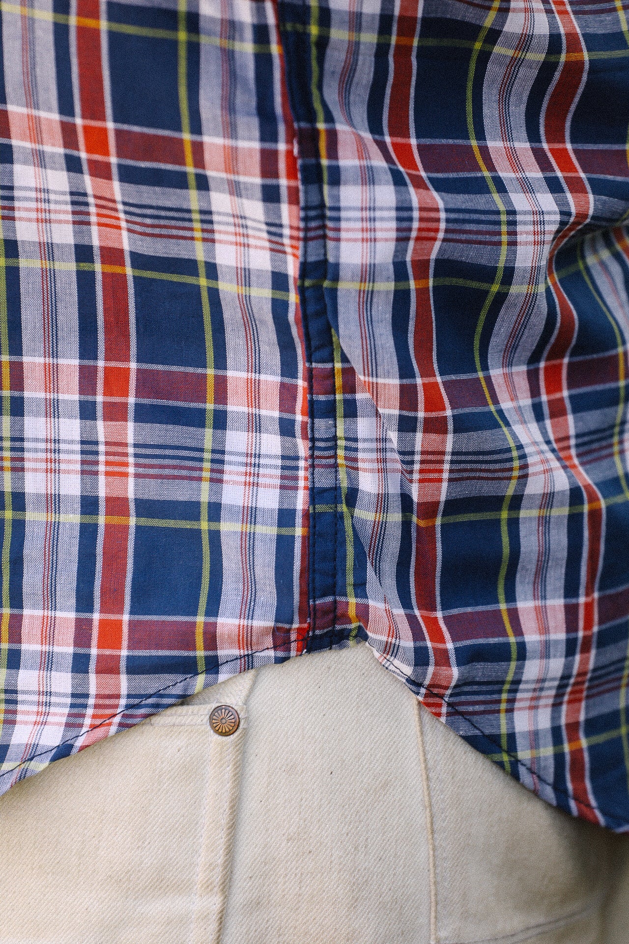 Close-up of navy madras plaid short sleeve shirt over light-colored denim pants with rivet detail