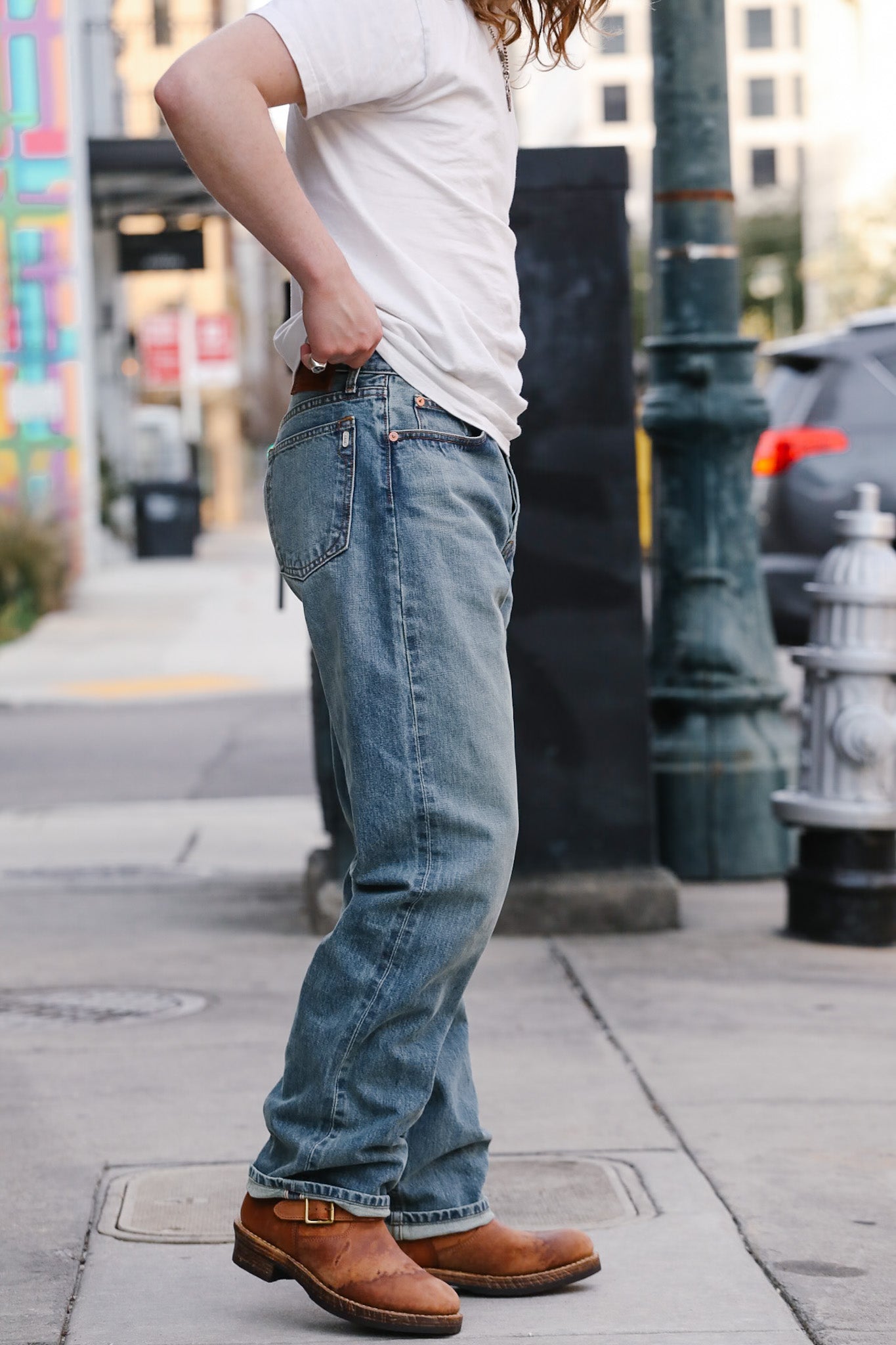 Person wearing blue jeans and brown shoes on a city street.