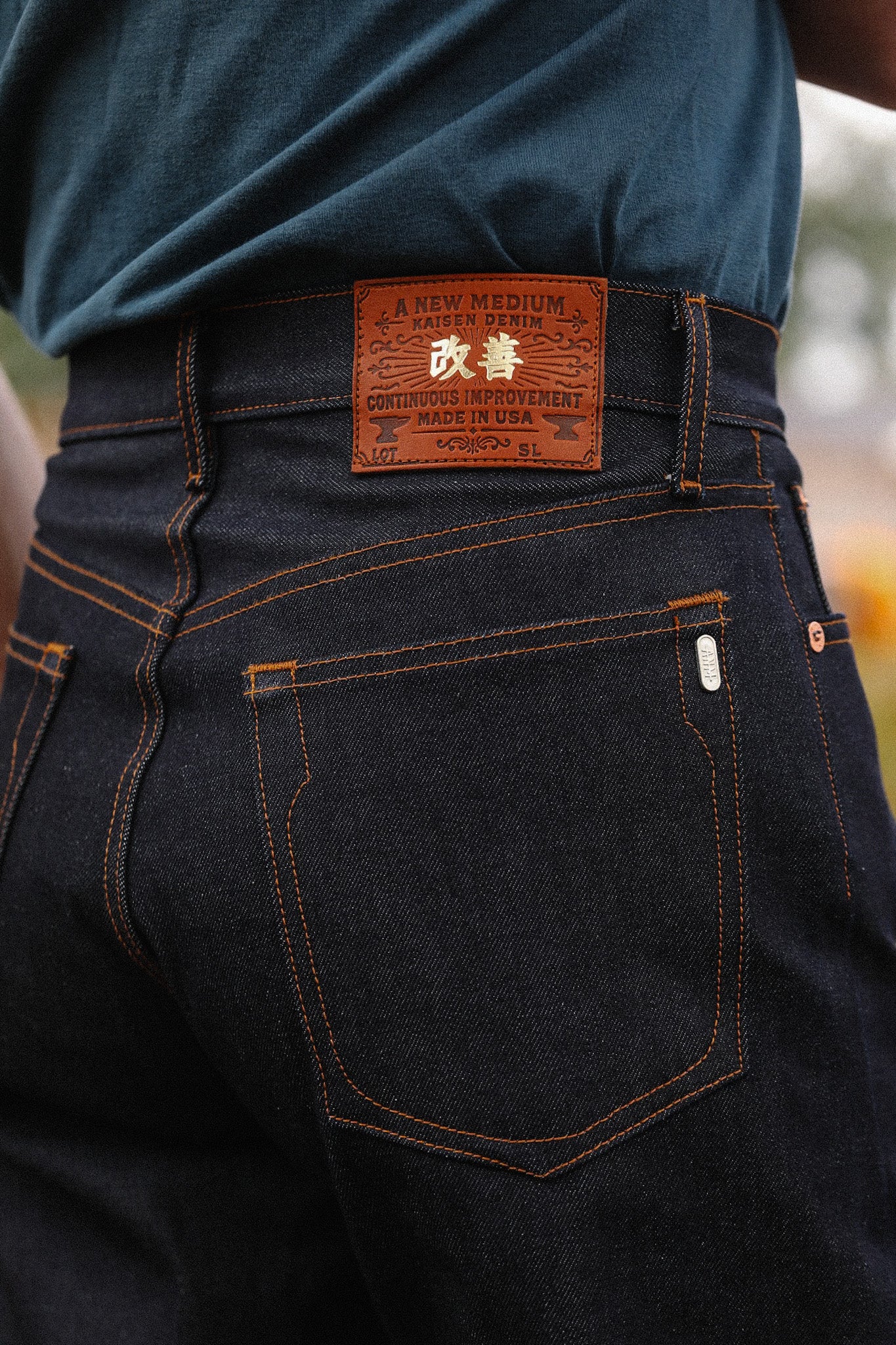 Close-up of dark indigo Kaisen Denim jeans with a brown leather patch and orange stitching