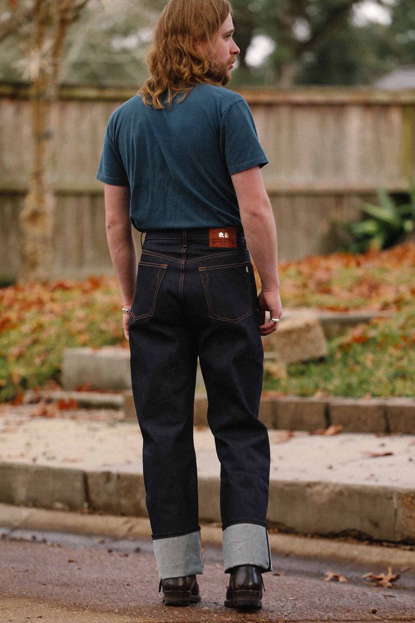 Man wearing wide straight 16.5oz Kaisen Indigo denim jeans with cuffs, dark teal t-shirt, and boots outdoors