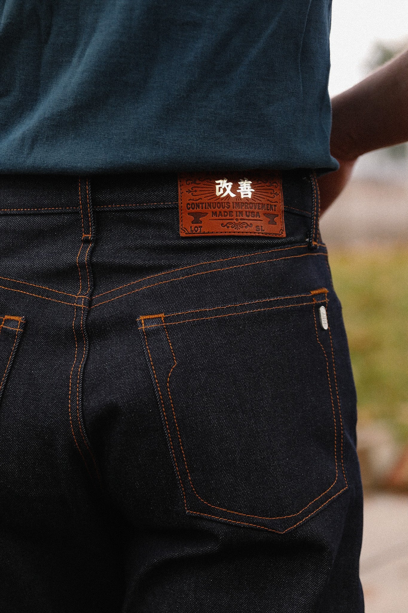 Close-up of indigo 16.5oz Kaisen denim wide straight jeans with orange stitching and leather patch detail