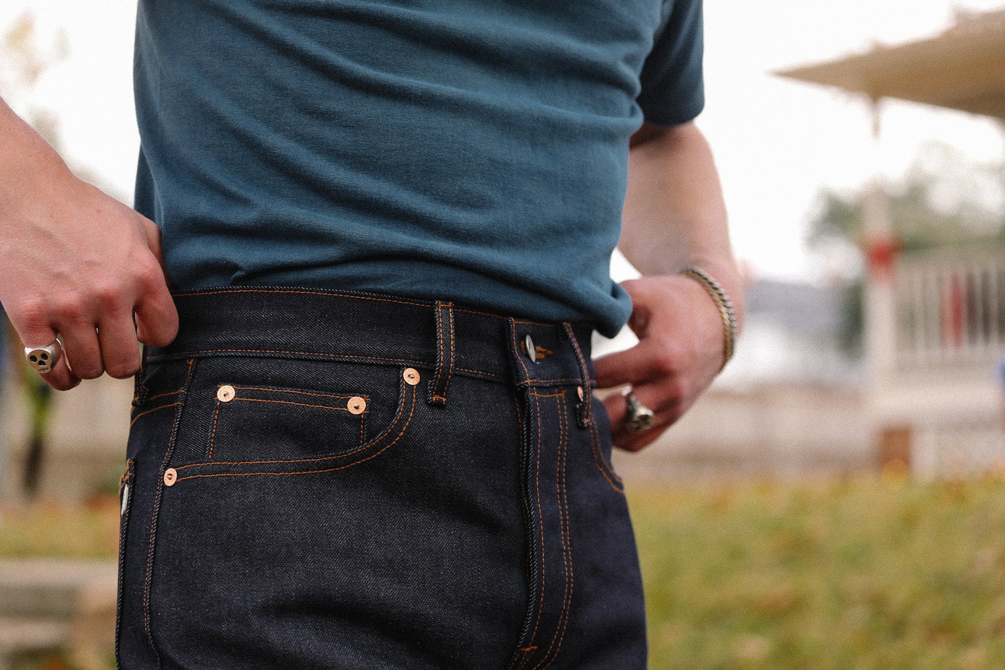 Person wearing dark indigo wide straight jeans with copper rivets and orange stitching outdoors